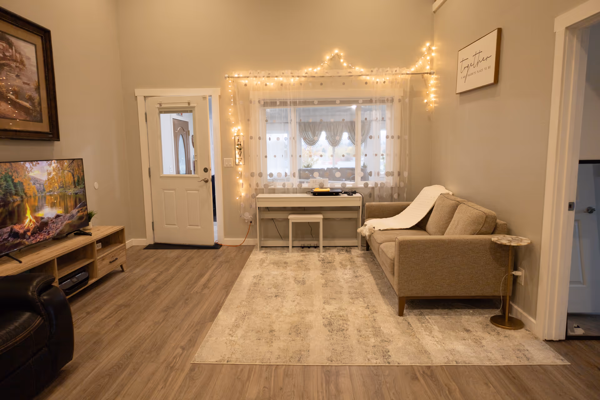 Cozy senior living lounge featuring a sofa, TV, string lights, and sheer curtains.