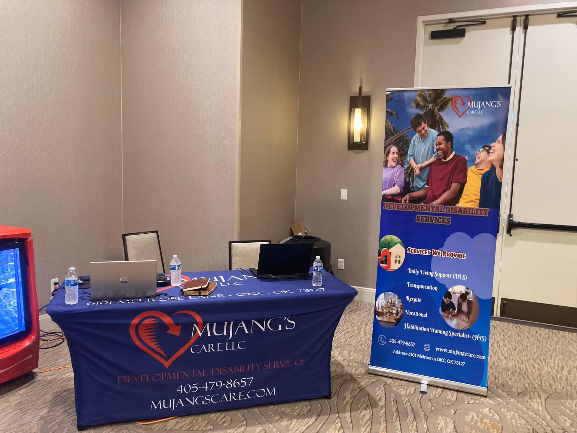 Indoor conference setup with Mujang's Care LLC banner and promotional table.