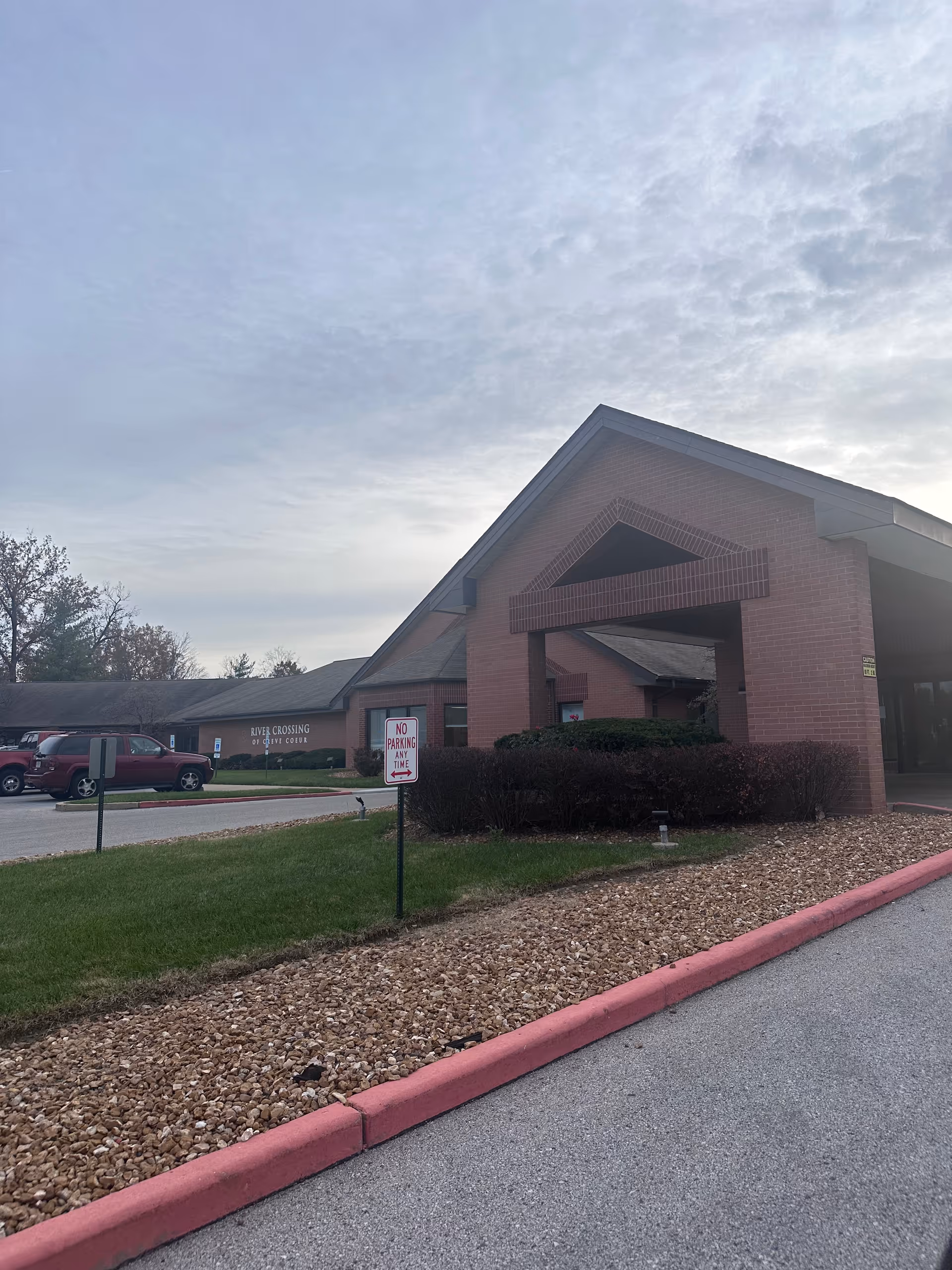 Brick entrance of River Crossing Rehab and Healthcare Center with a covered drive-through canopy, parking area, and a 'No Parking' sign.