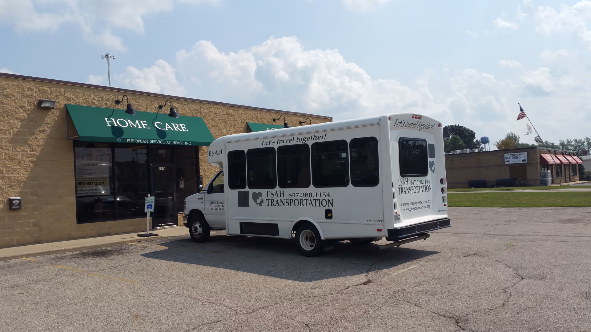 White transportation van parked in front of a beige building with a green Home Care awning.