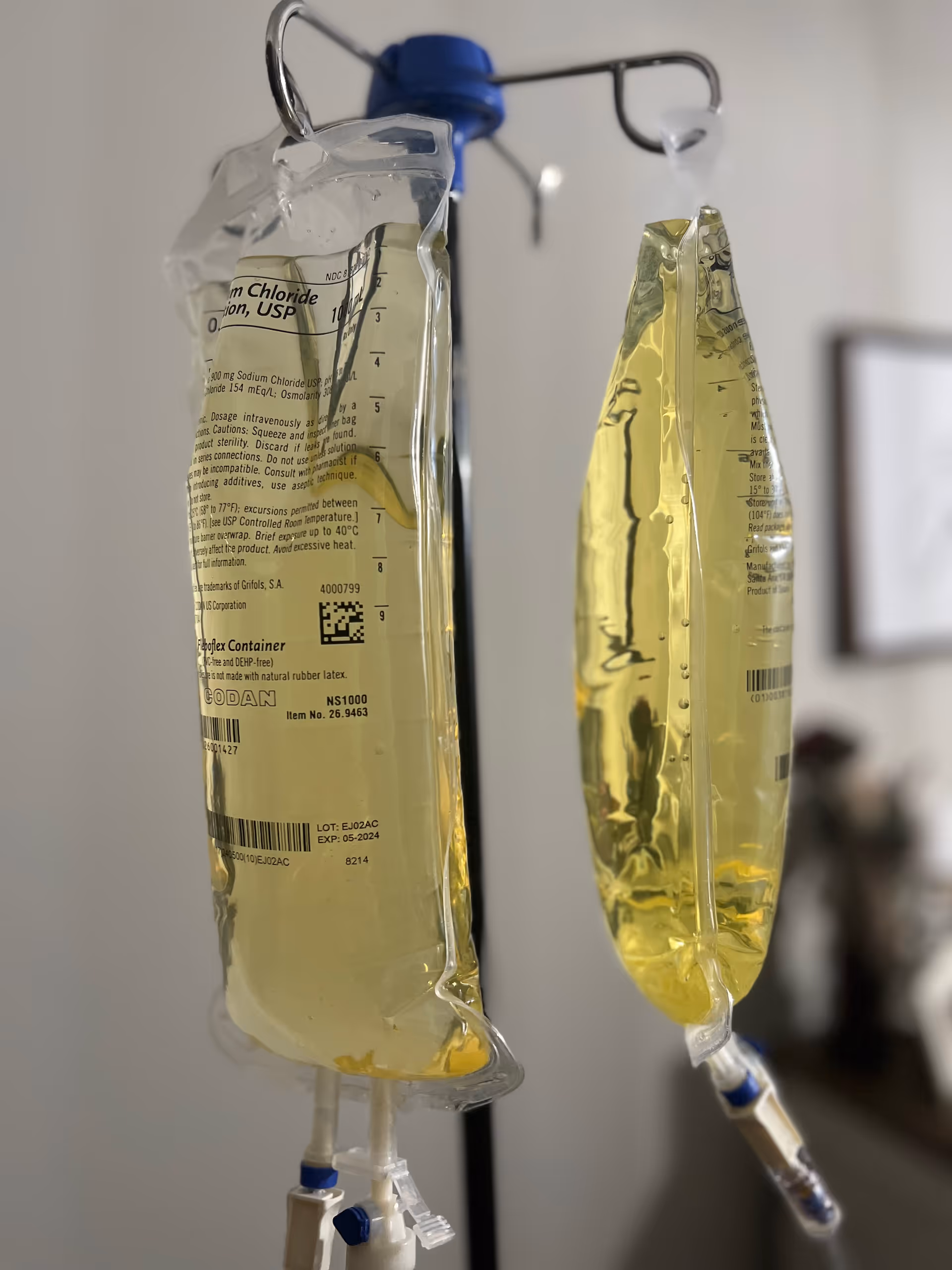 Two IV bags hang from a stand in a clinical indoor setting.