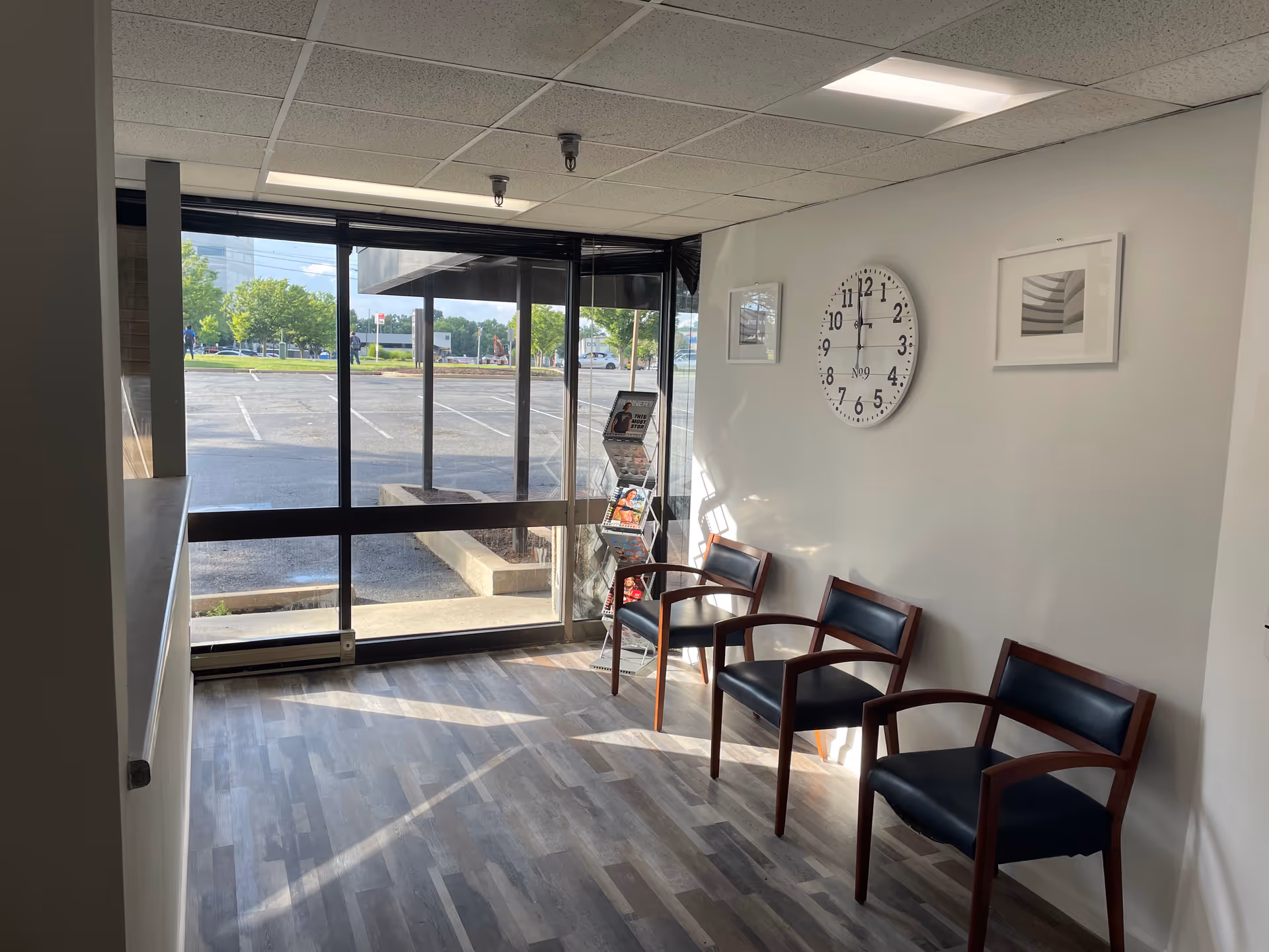 Bright interior lobby with four chairs, large glass windows, and a wall clock.