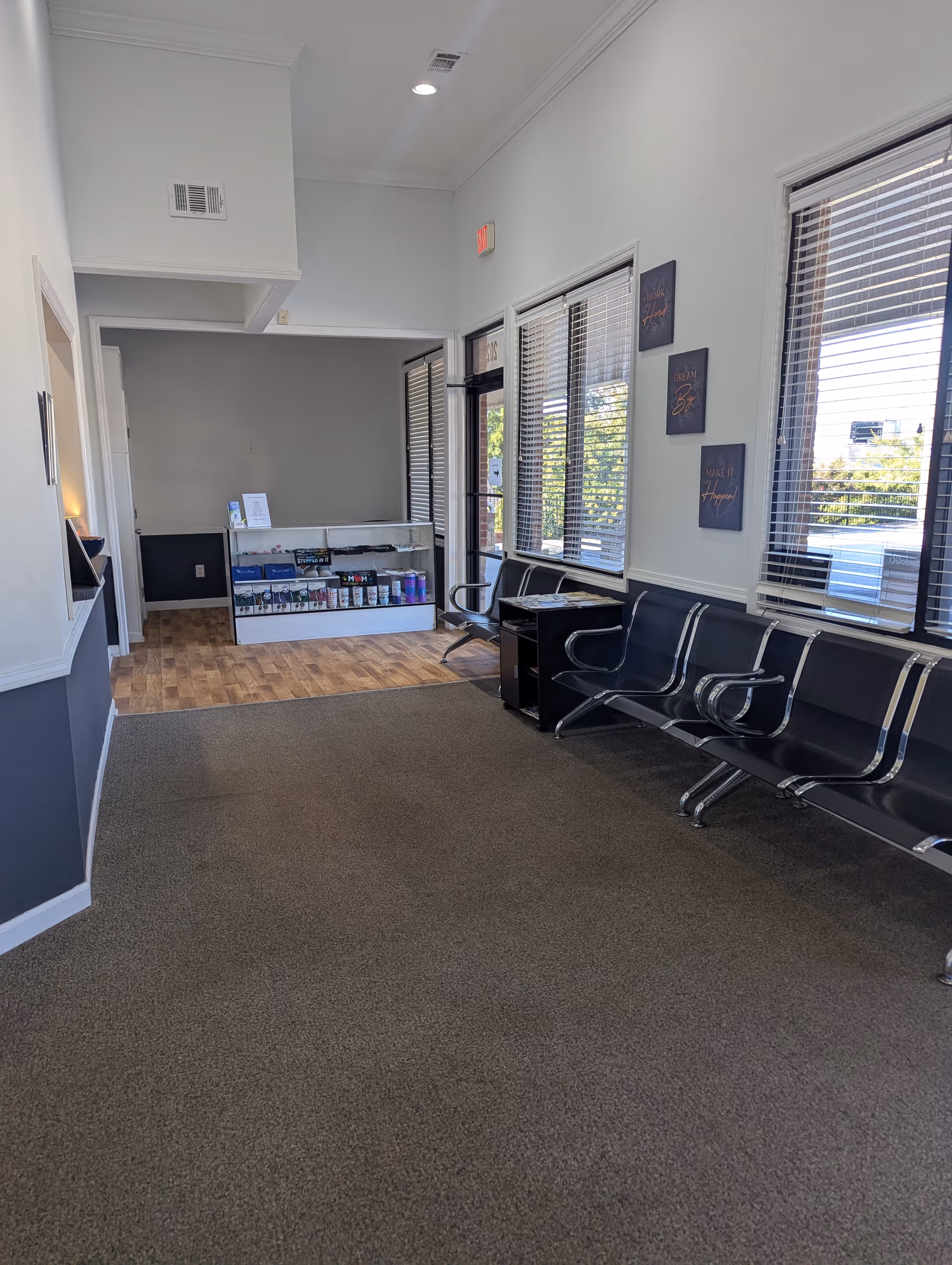 A waiting lobby with black chairs along a wall and a reception desk in back.