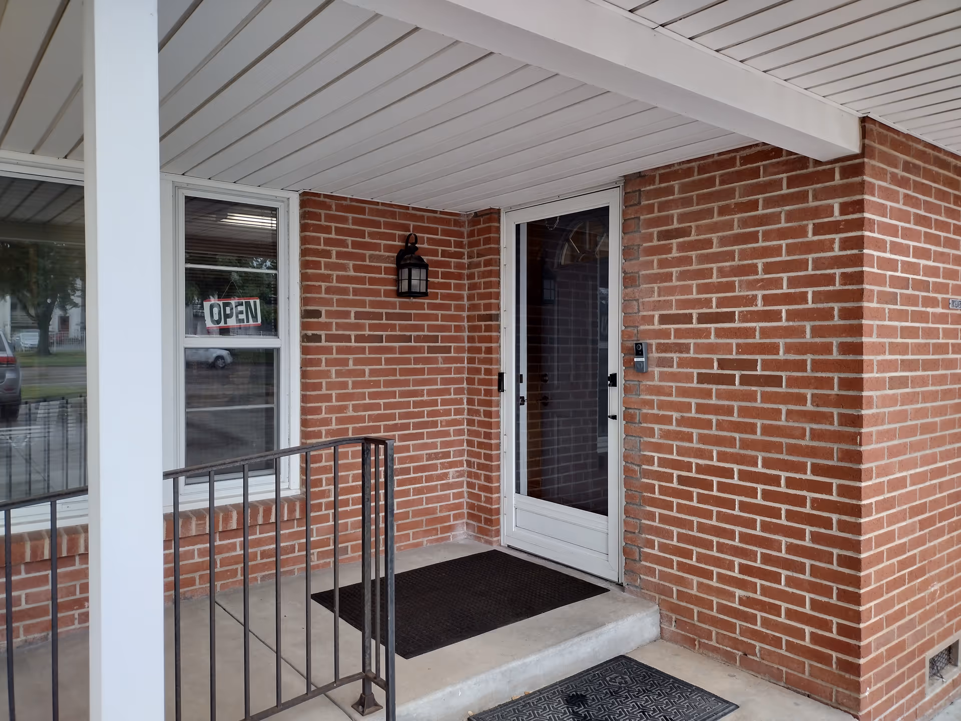 Brick exterior entrance with a glass door, window, and an open sign.