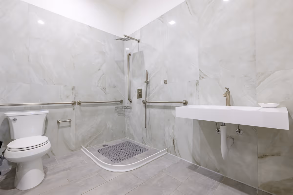 Accessible bathroom featuring wall-mounted sink, toilet, and curved-entry shower with grab bars.