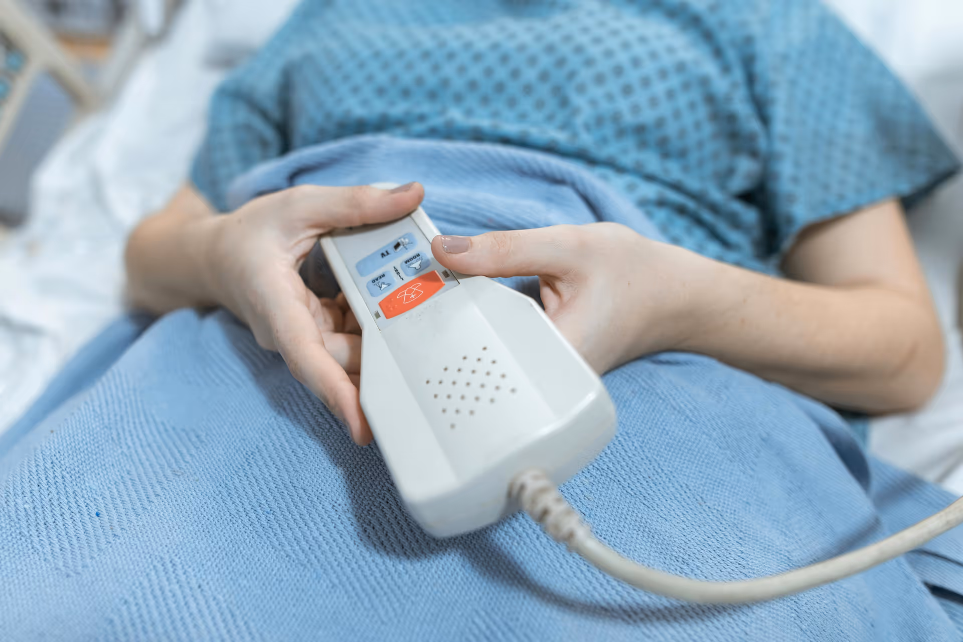 Close-up of a patient in a blue gown holding a hospital call button.