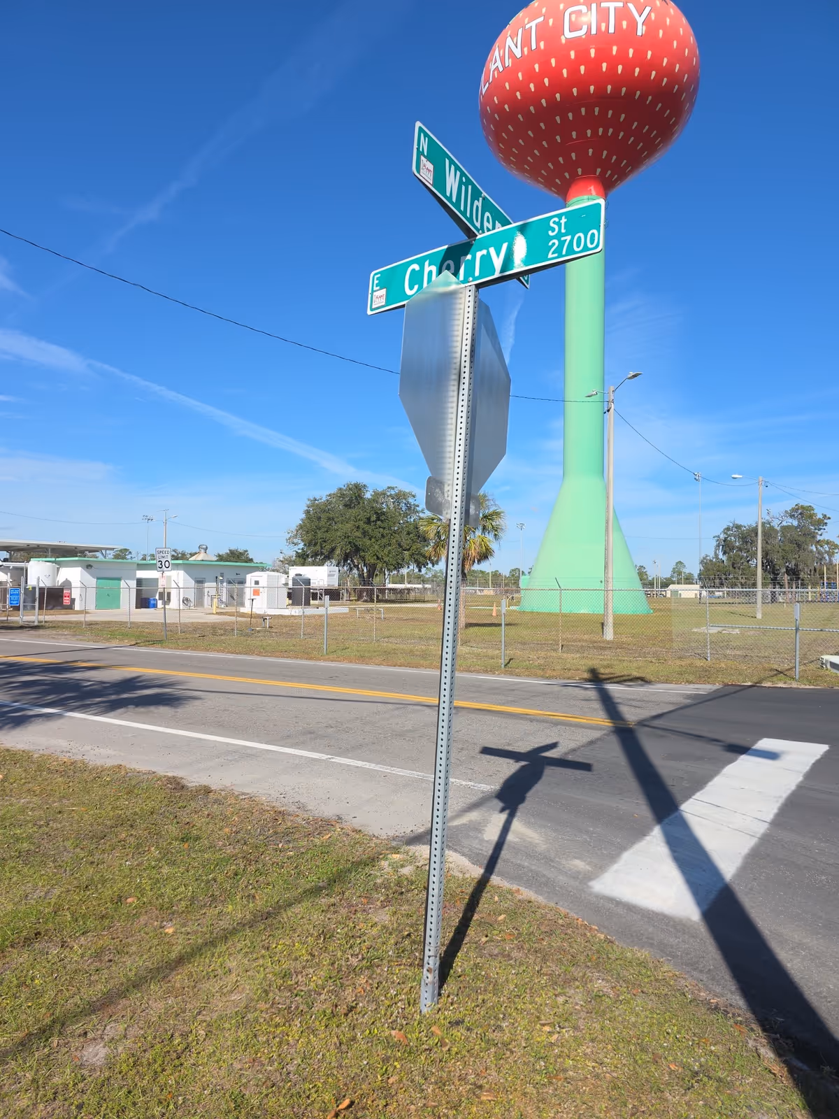 Green street signs at a corner with a tall red water tower against a clear sky.