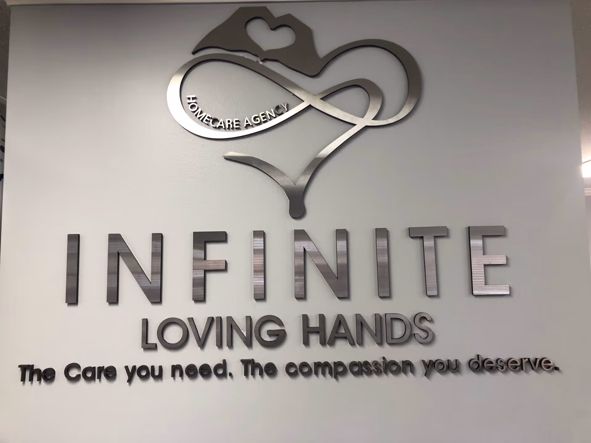Interior wall sign displaying Infinite Loving Hands logo and tagline on a gray wall.