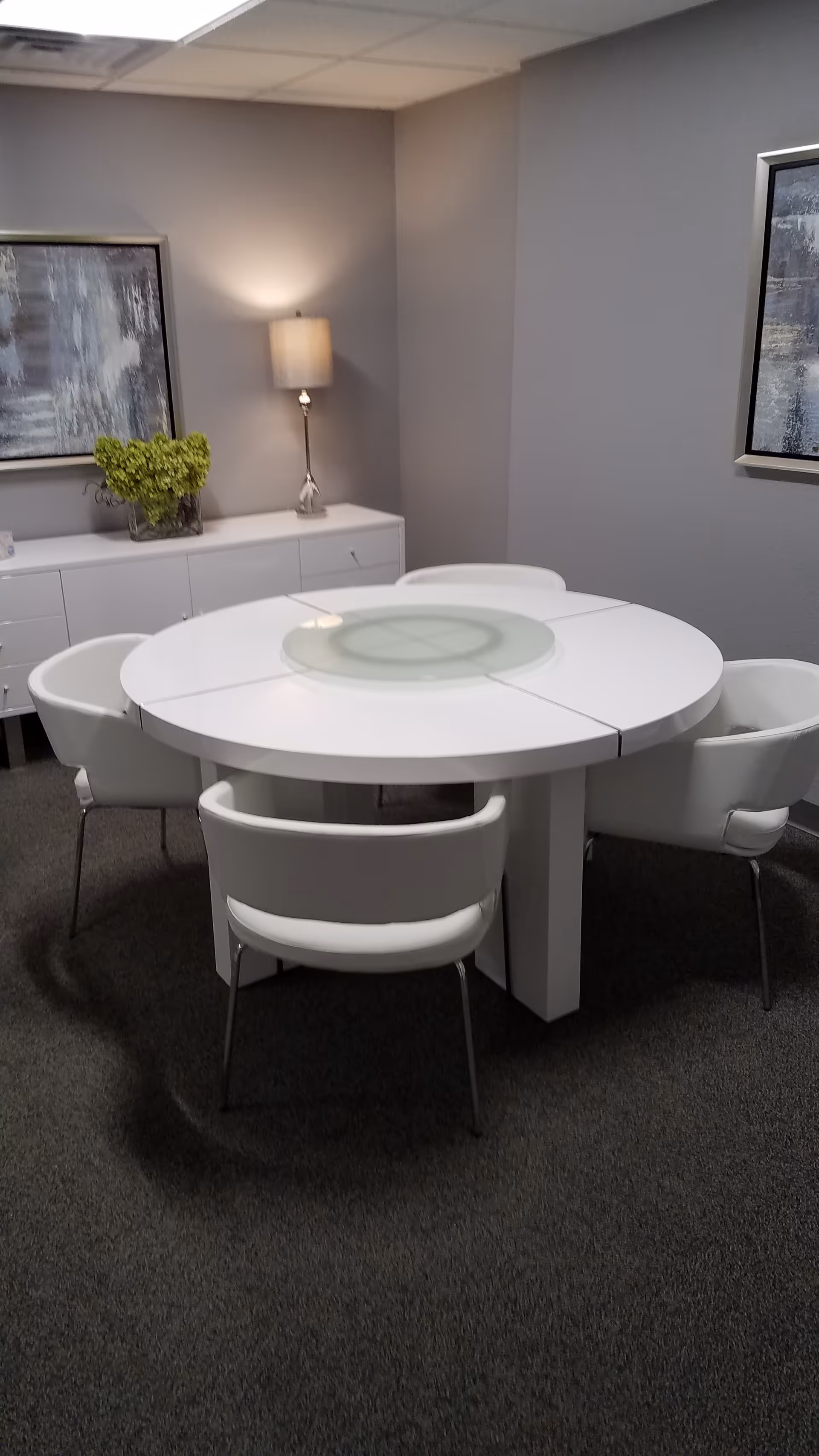 White round dining table with glass centerpiece and white chairs in an elegant, quiet dining room.