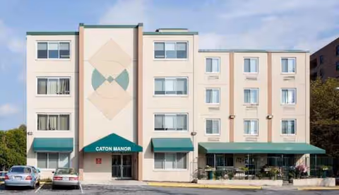 Three-story beige nursing home with green awnings and a parking lot in front.
