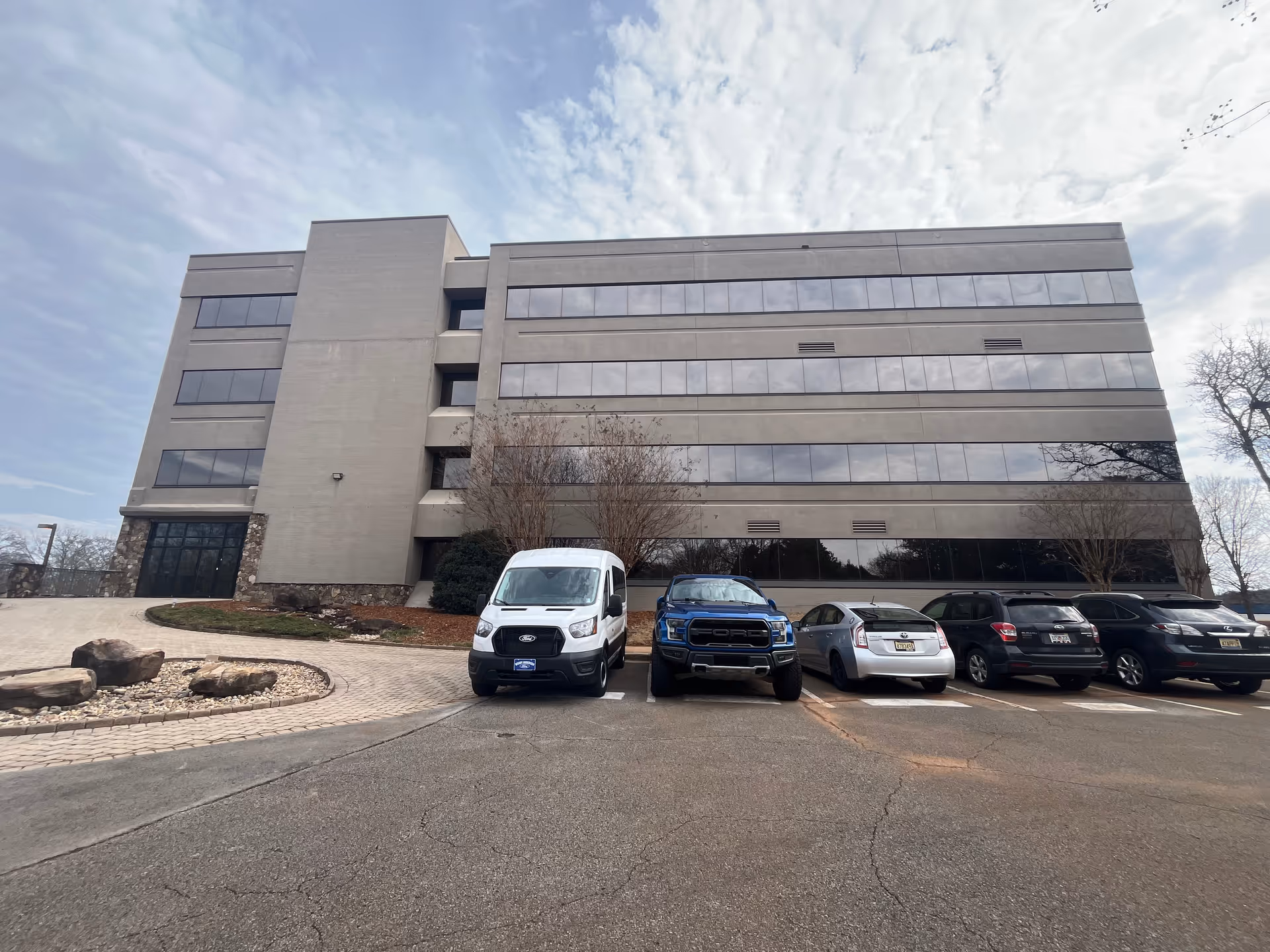 Modern, multi-story CareCo facility with a parking lot in front and a cloudy sky.