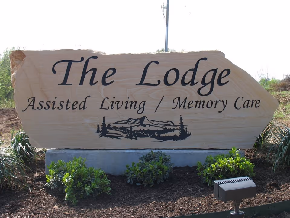 A large stone sign reading The Lodge: Assisted Living / Memory Care, outdoors with landscaping.