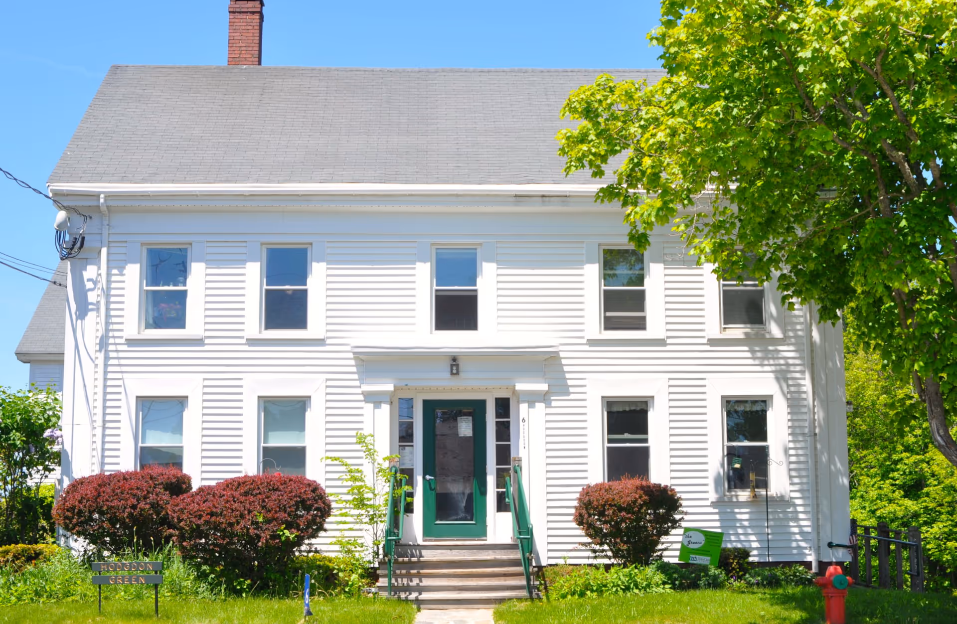 White two-story building with green door, steps, shrubs, and a Hodgdon Green sign.
