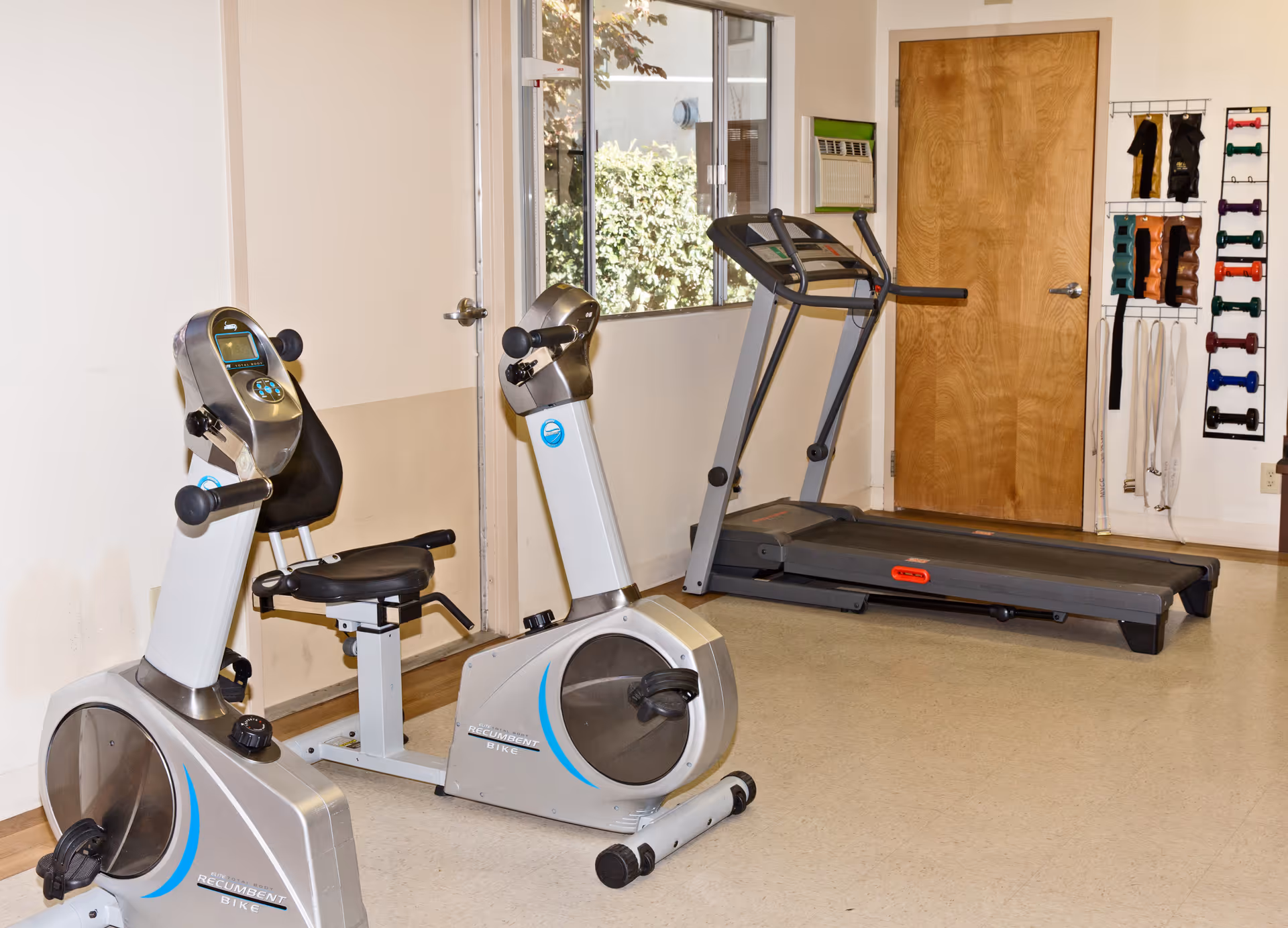 Interior fitness room with treadmills, exercise bikes, and weight rack in care facility