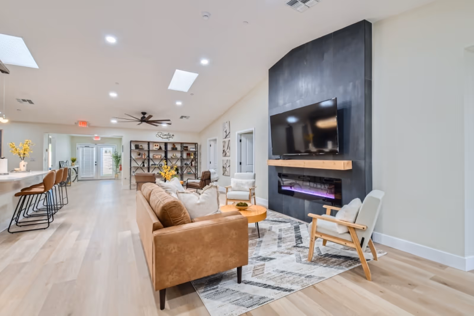 Spacious modern senior living lounge with sofa, chairs, fireplace, and wall-mounted TV.
