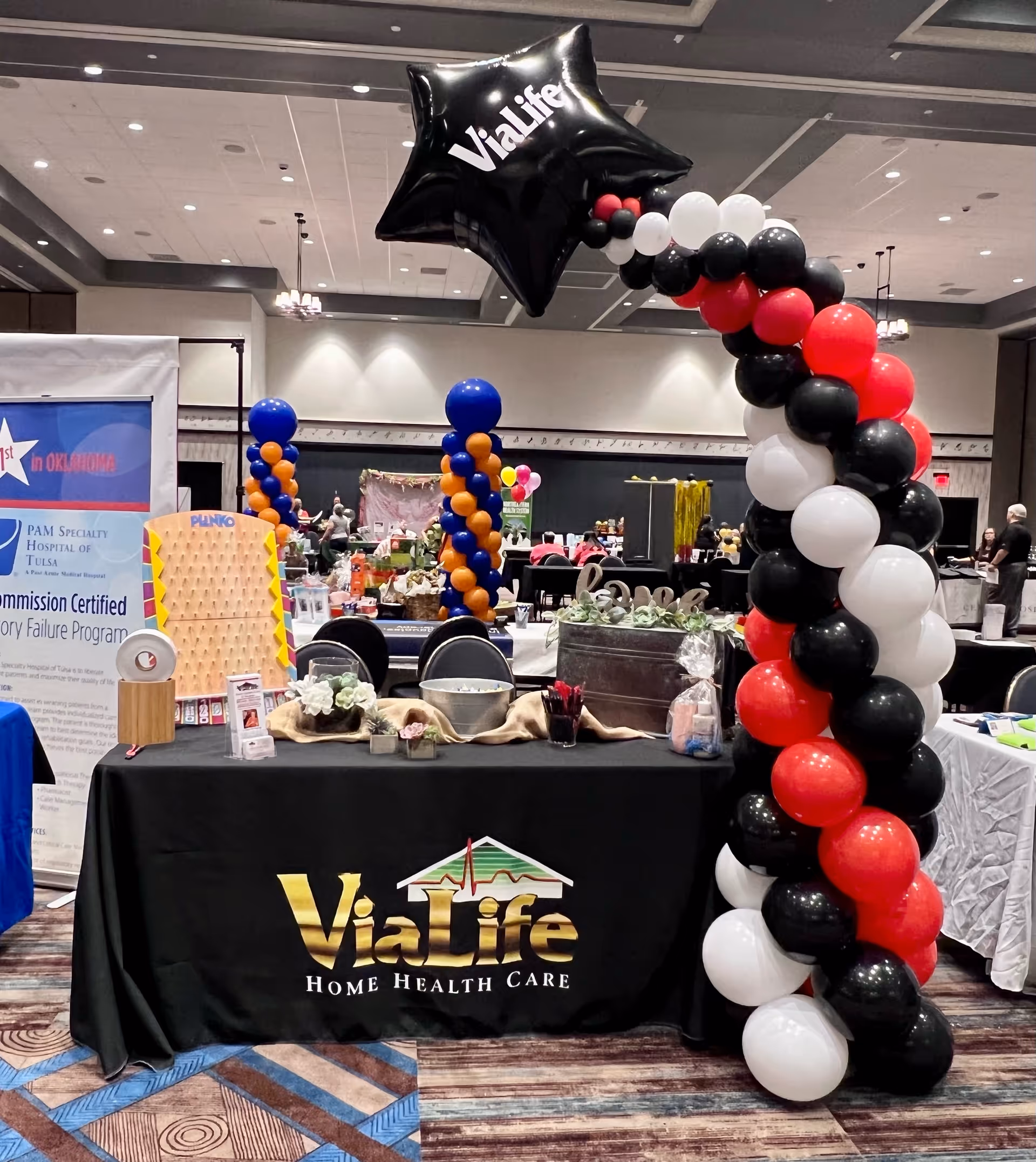 Trade show booth for ViaLife Home Health Care with balloon arch and table display.