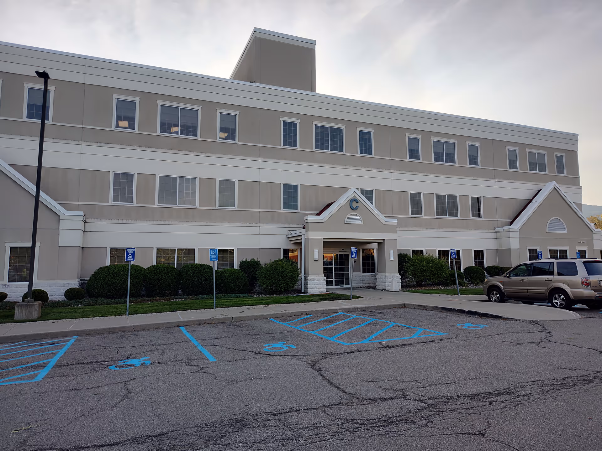 Exterior view of a beige medical rehabilitation facility with parking, handicap spots visible