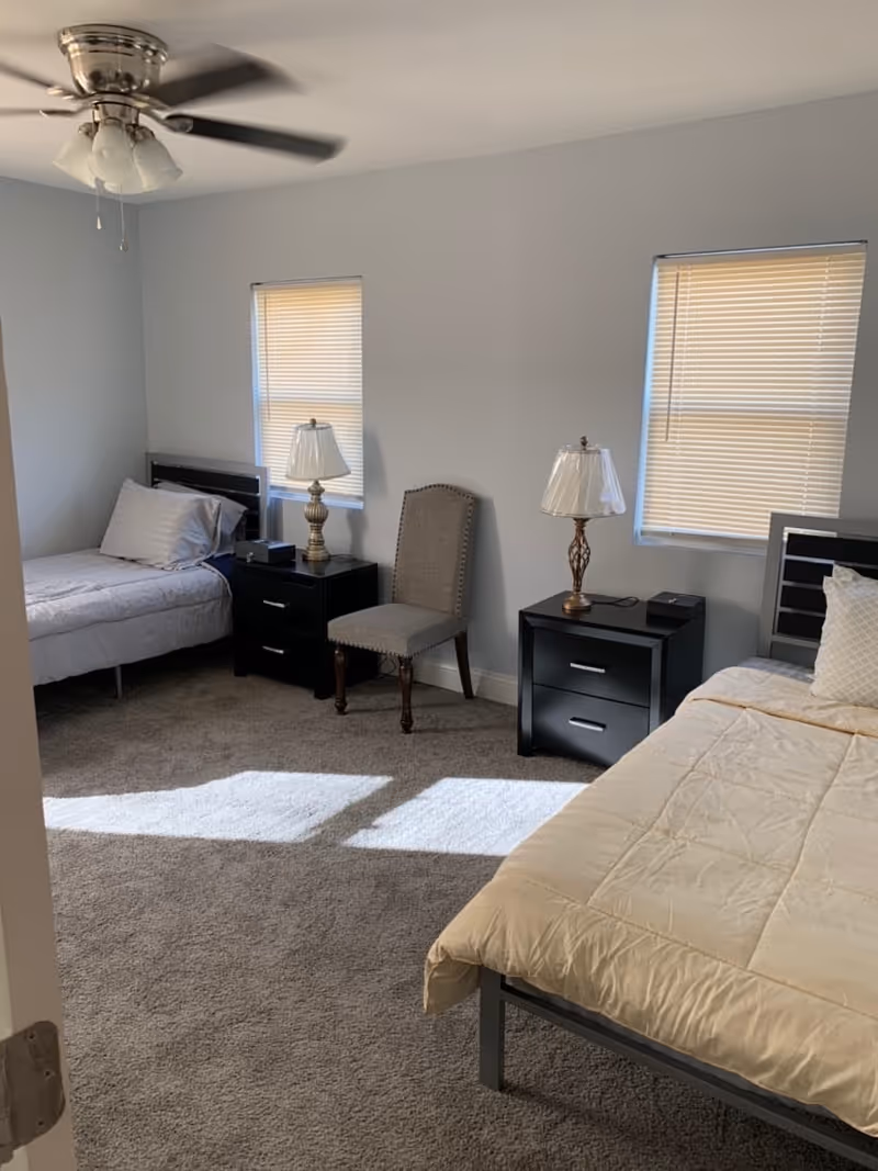 Two beds with nightstands and lamps in a clean, neutral-toned bedroom.