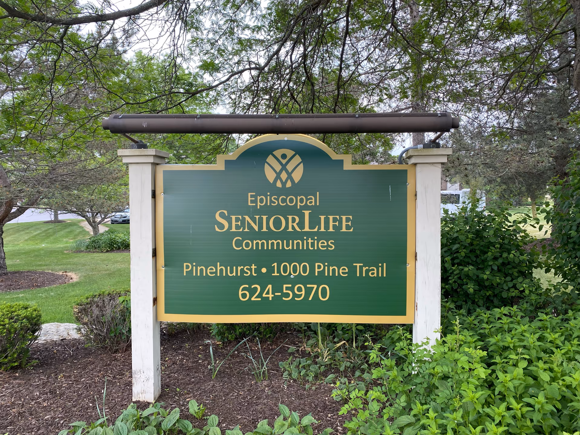 A green sign with gold lettering for Episcopal SeniorLife Communities Pinehurst among shrubs.