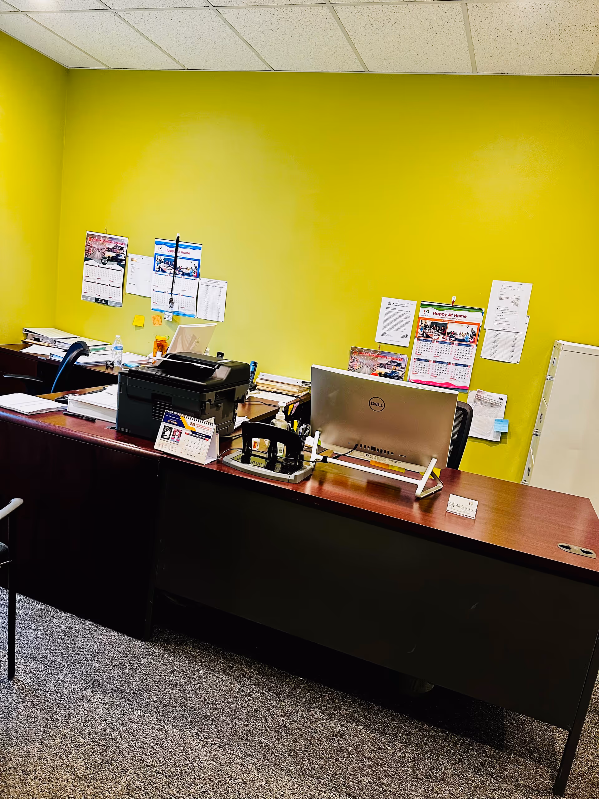 Bright lime-yellow wall behind a desk with computer, printer, and bulletin boards.