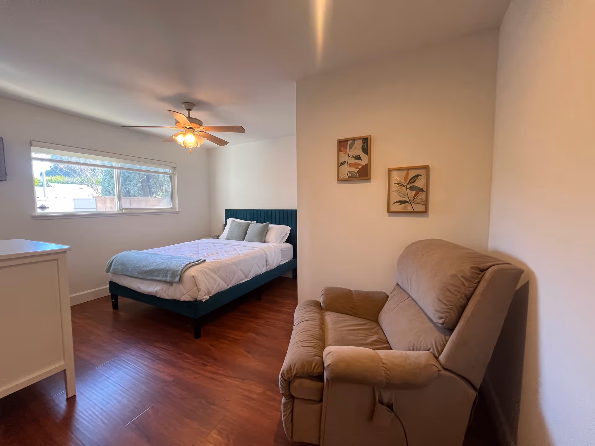 Bright bedroom with a bed, dresser, and beige recliner in a tidy room.