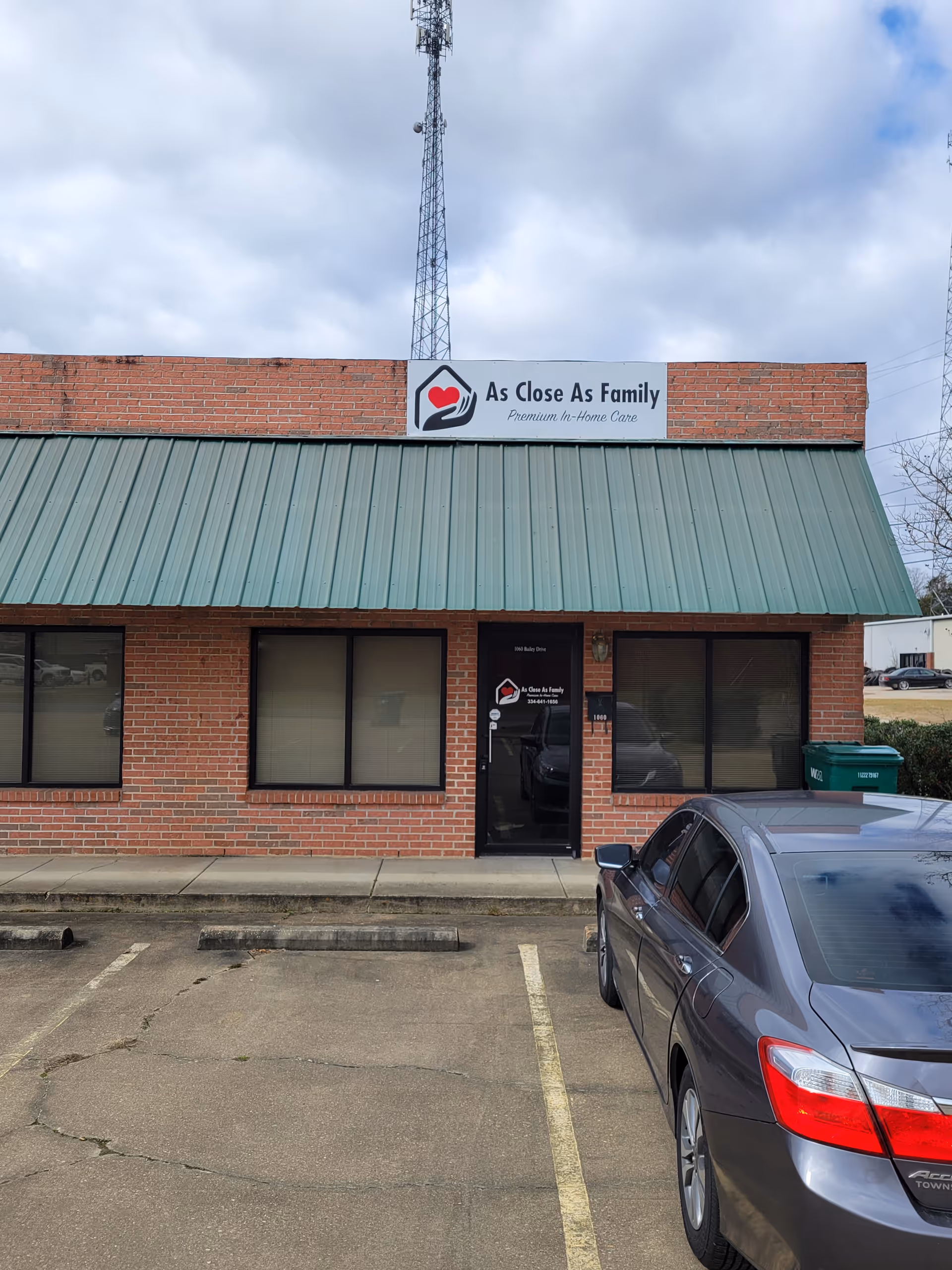 Brick building with a green metal roof, signage reading As Close As Family, parking lot.