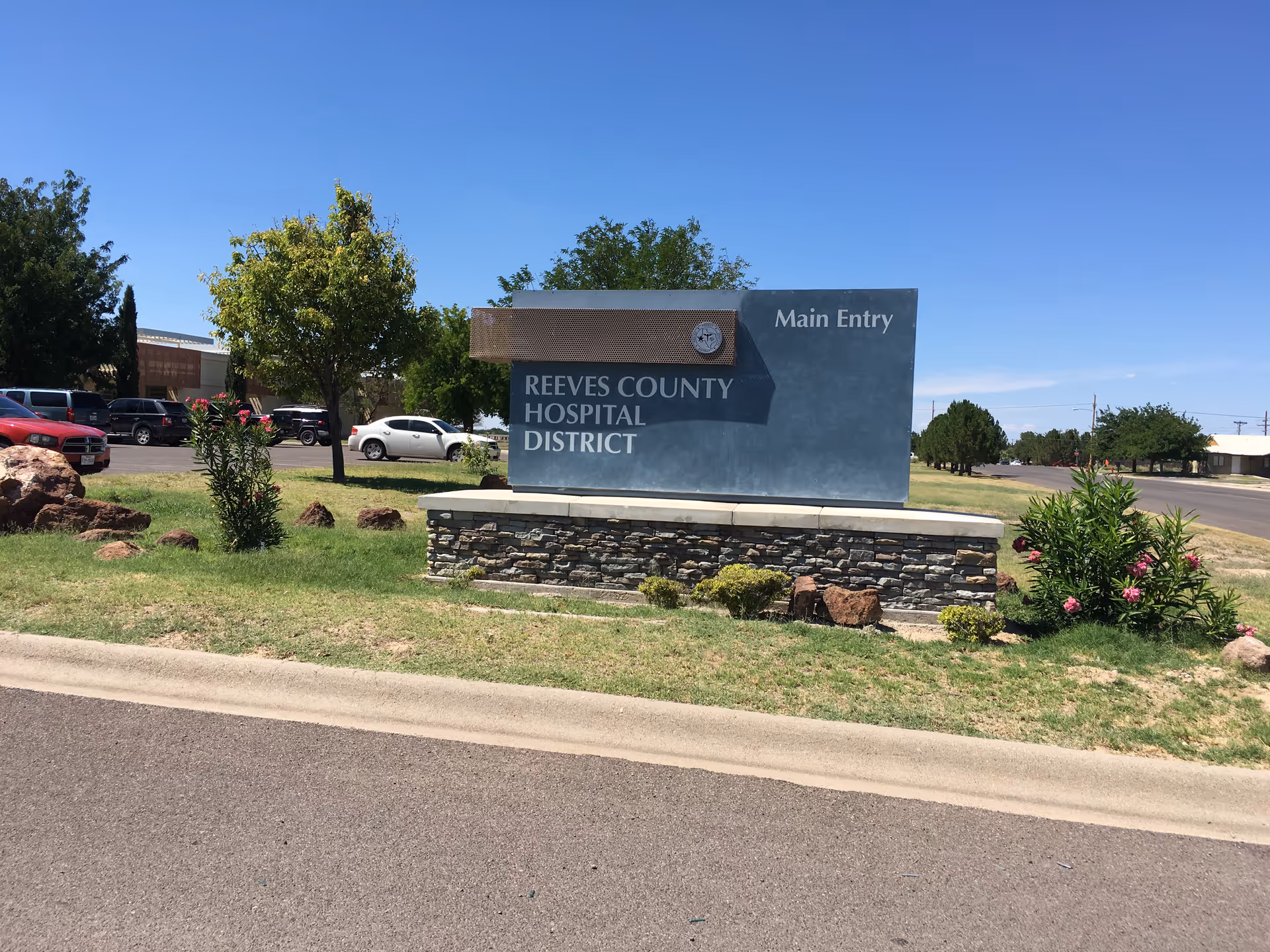 Exterior view of Reeves County Hospital District Main Entry sign with cars in the parking area.