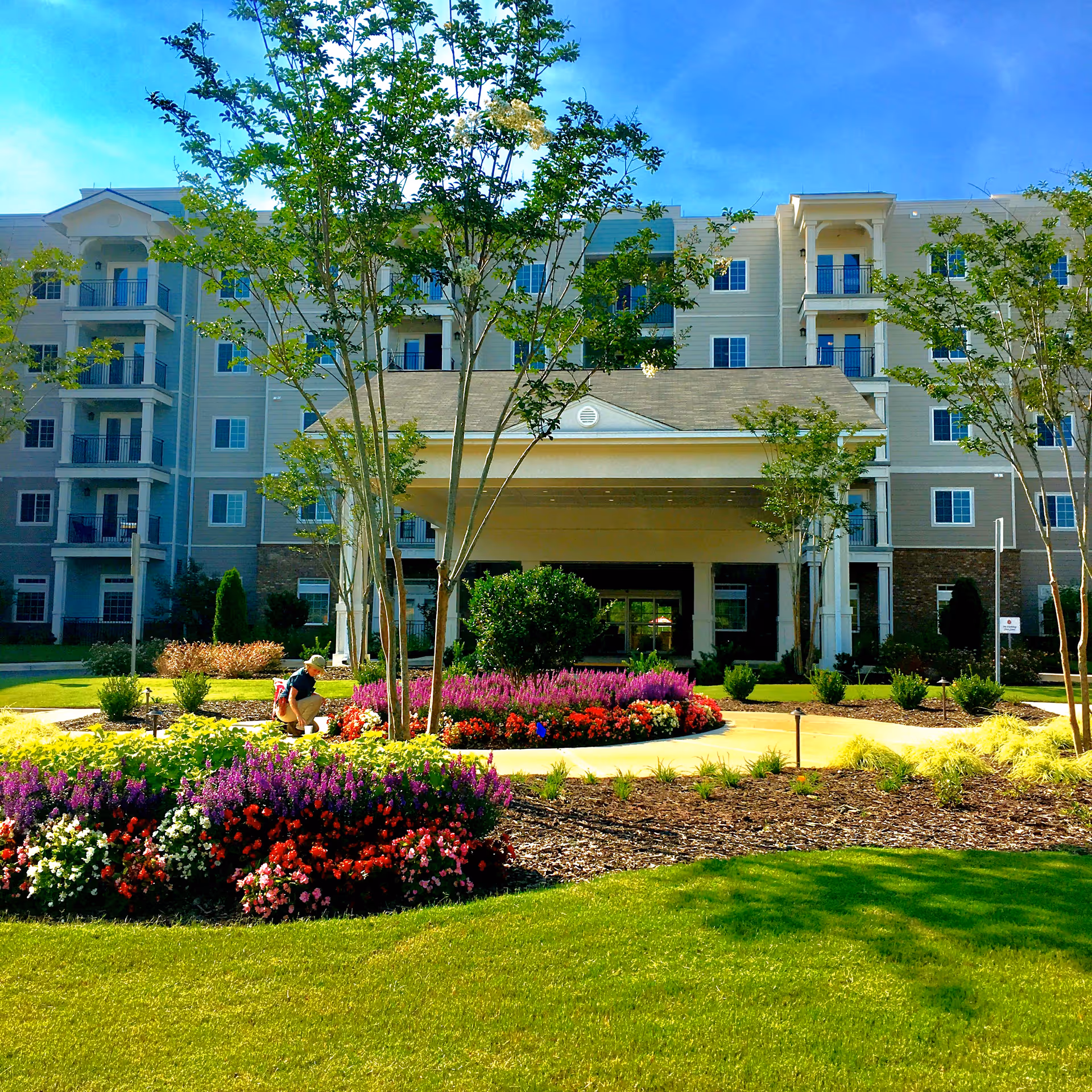 Multi-story senior living building with landscaped garden and colorful flower beds in foreground.