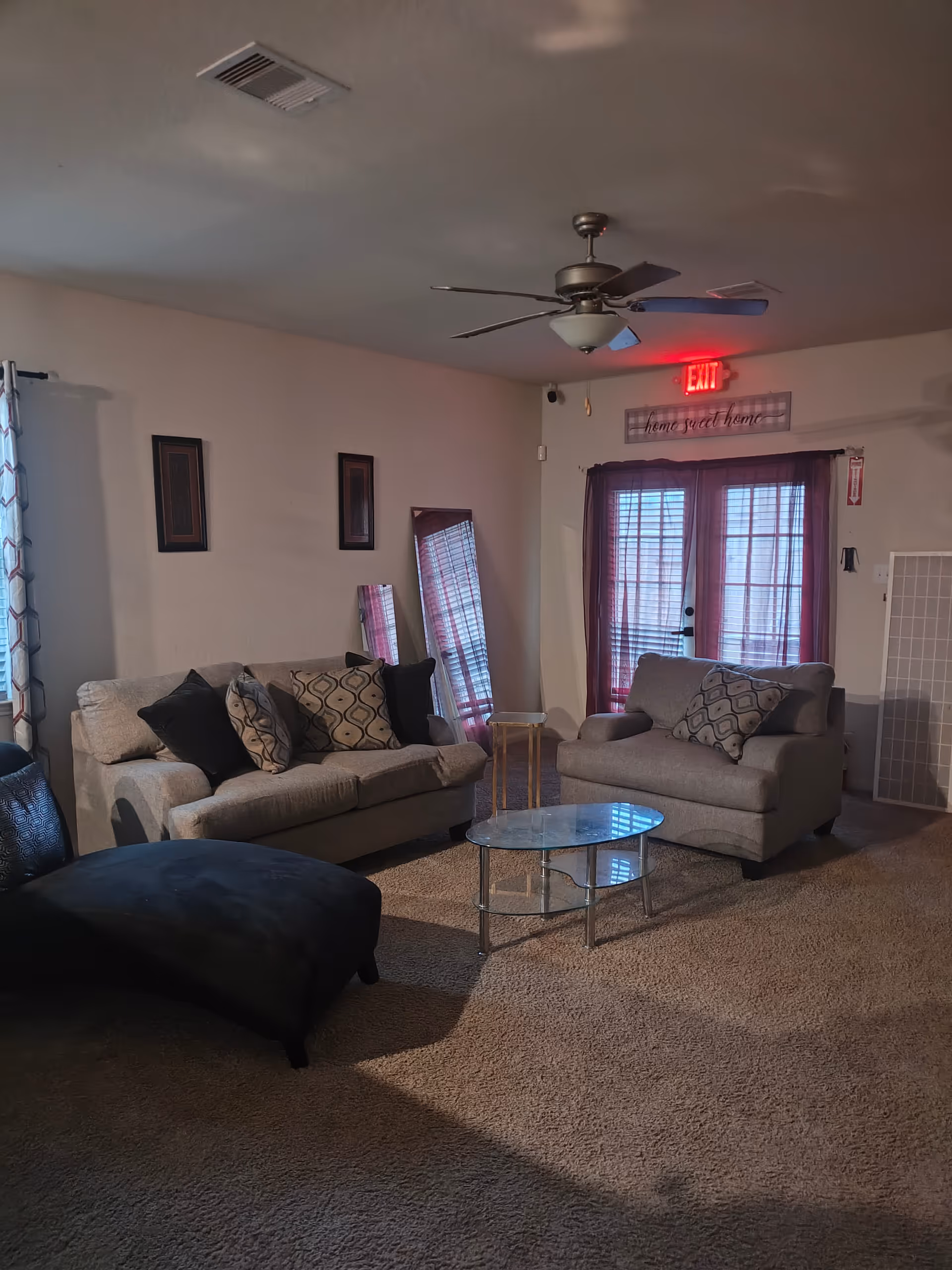 Cozy living room in a senior facility with beige sofas, glass coffee table, and red curtains.