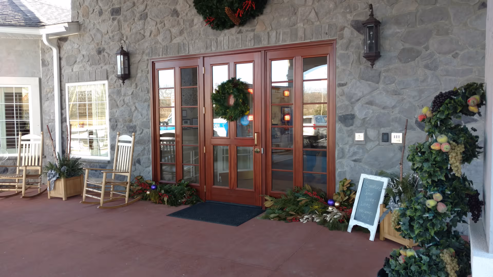 Stone facade with wooden double doors, wreaths, and rocking chairs on a porch.