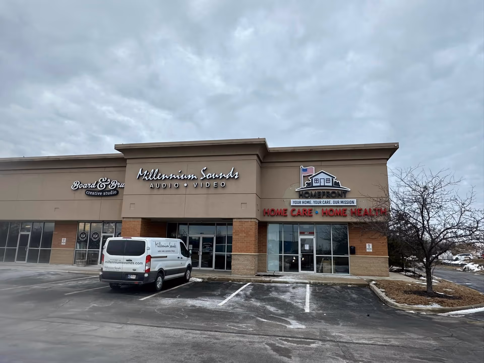 Exterior of a shopping plaza featuring Homefront Home Care sign and neighboring shops with a van.