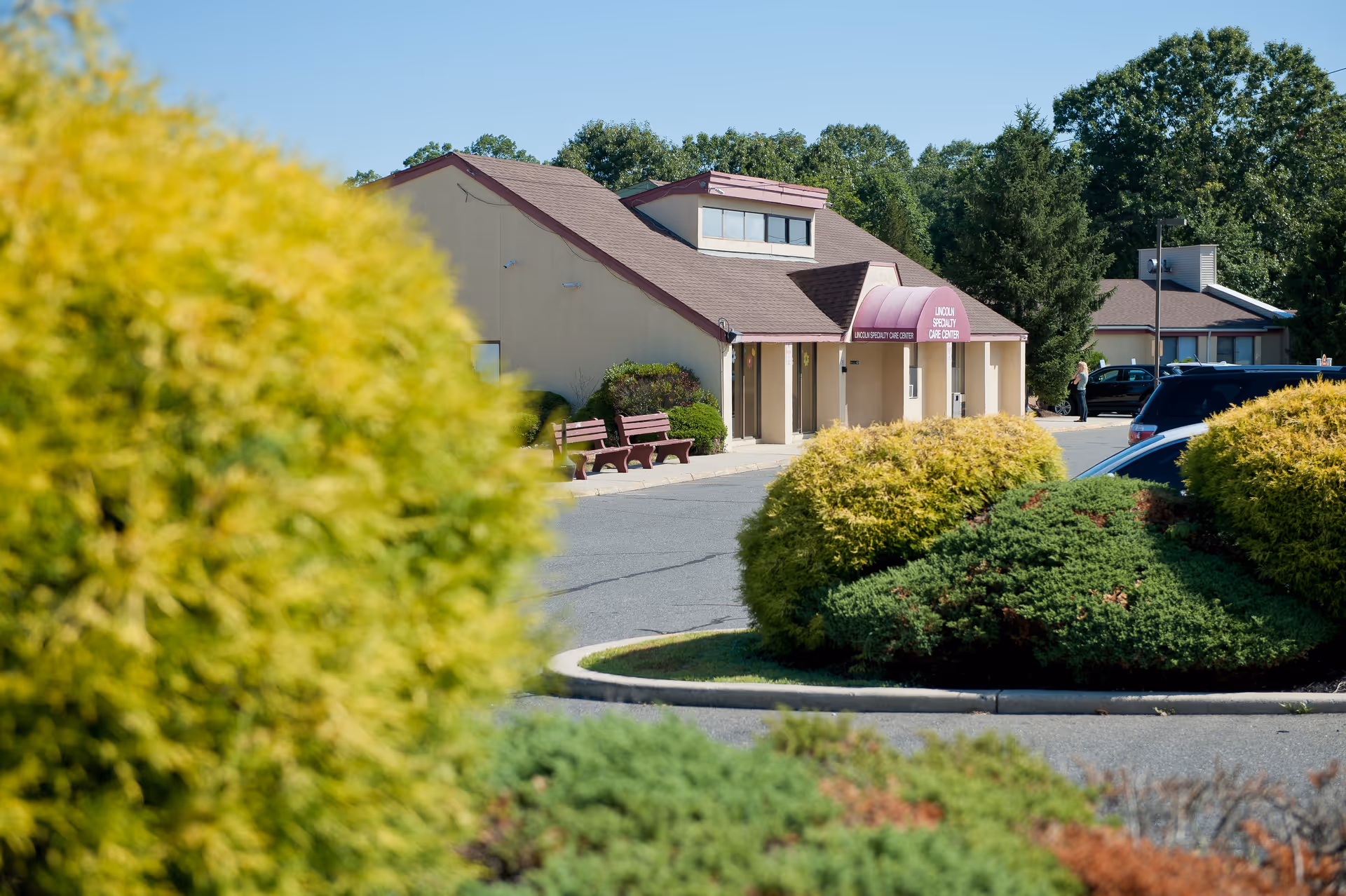Exterior view of Lincoln Specialty Care Center with shrubs, benches, and cars in the parking lot.