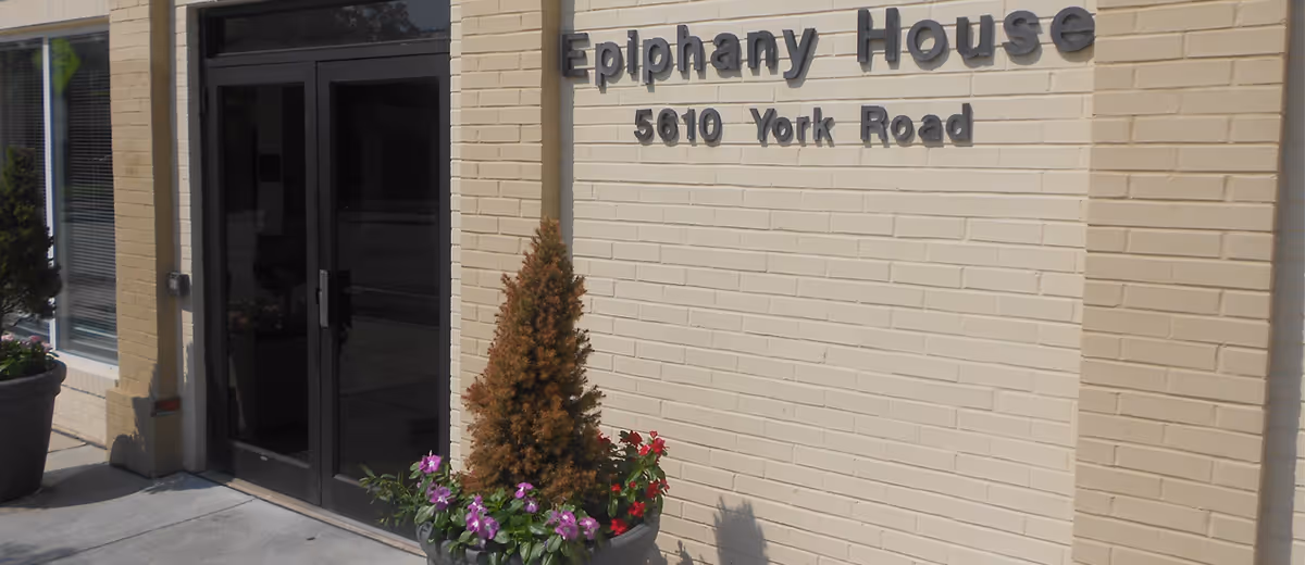 Exterior view of Epiphany House facility entrance with brick facade and potted plants.