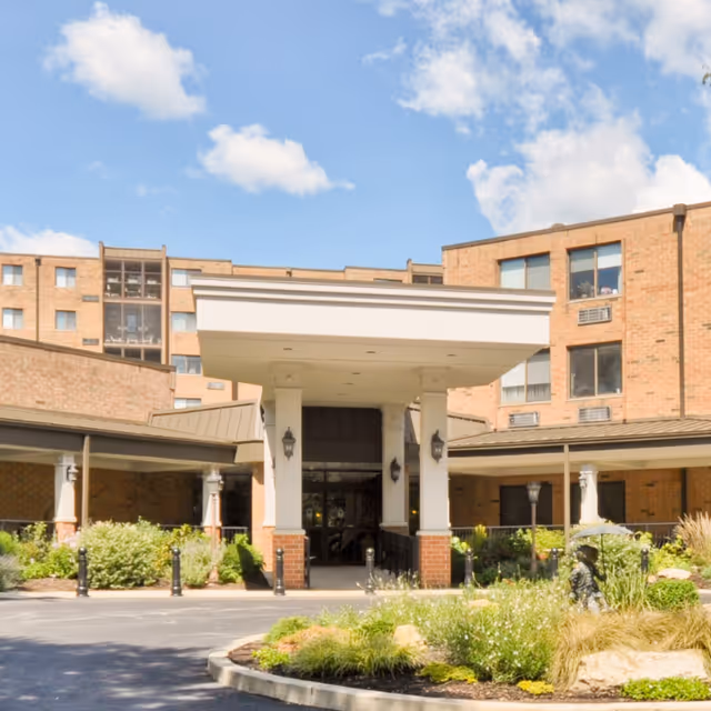 Brick senior living facility entrance with a covered porte-cochère and landscaped approach.