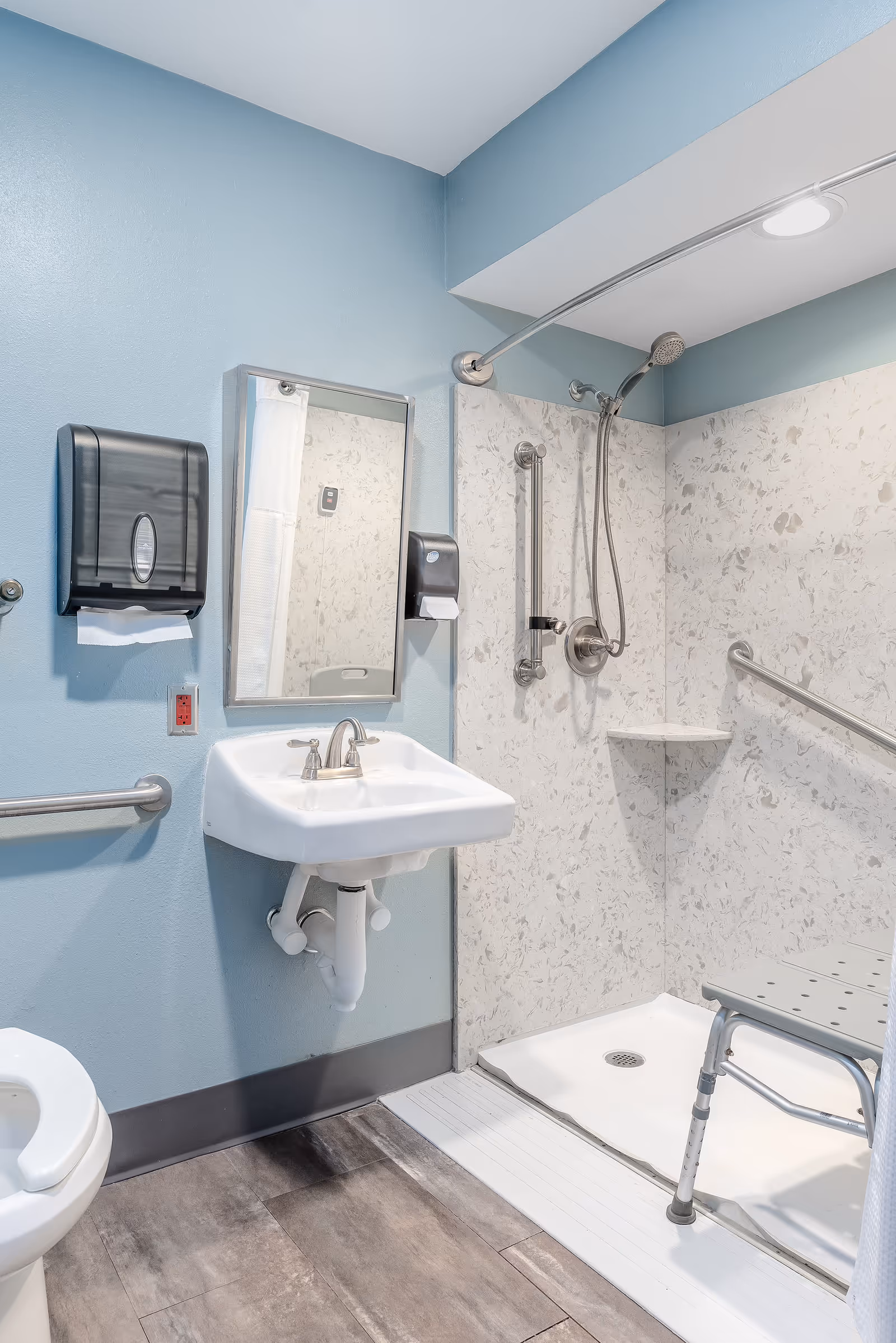 Accessible bathroom in a senior care facility with sink, mirror, shower, and grab bars.