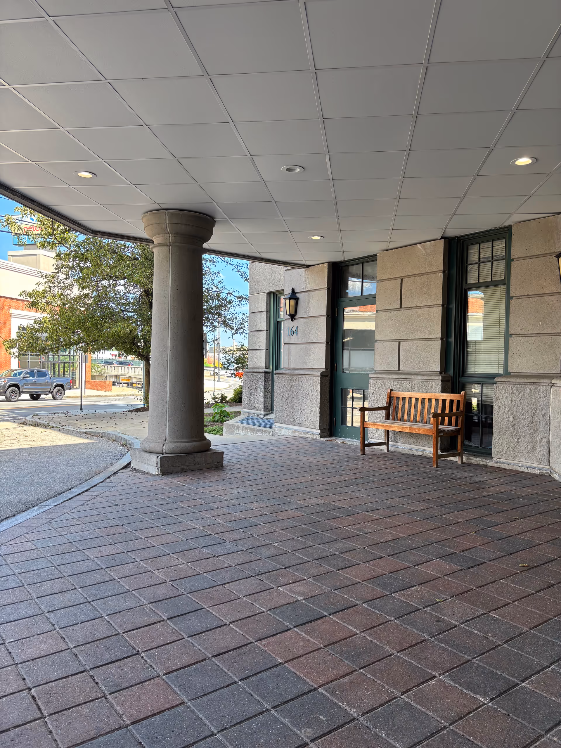 Covered entrance of Assisted Living Residences at Hancock Park with a wooden bench outside