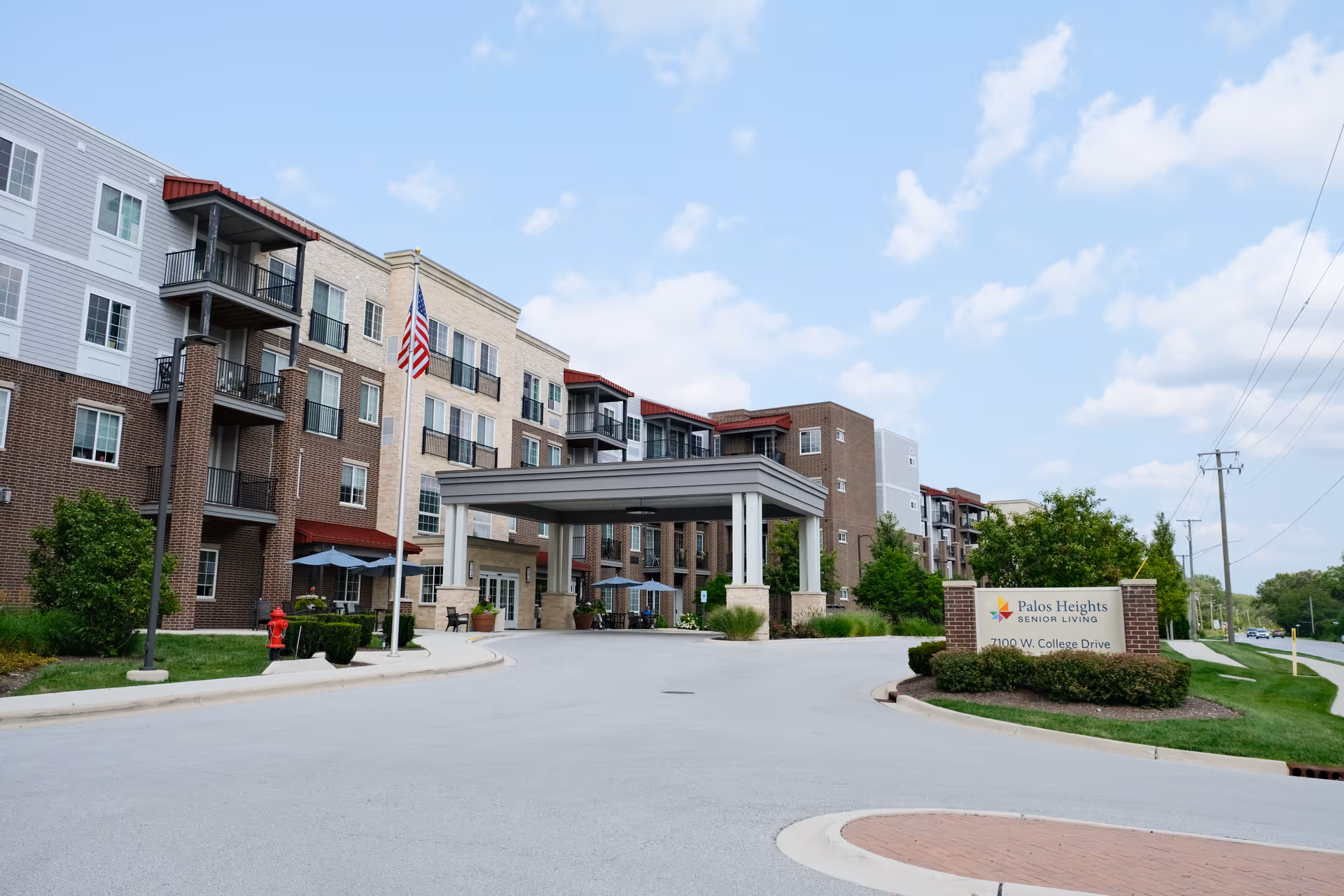 Front entrance and driveway of a multi-story senior living building with a covered porte-cochere and a sign reading 'Palos Heights Senior Living'.