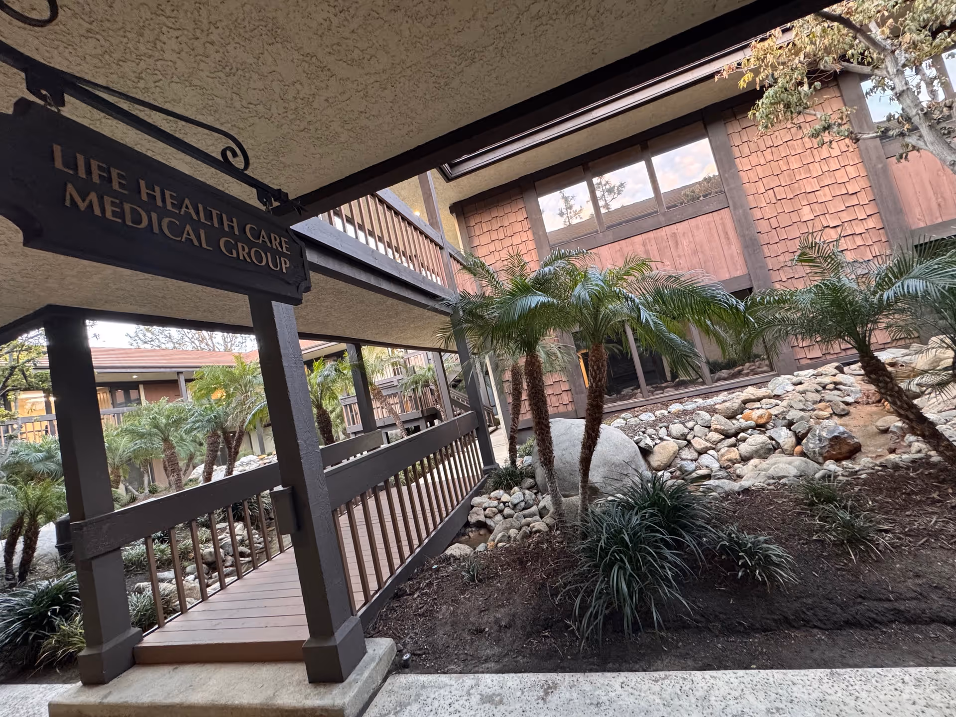 Exterior view of Life Health Care Medical Group entrance with palm trees and landscaped rocks.
