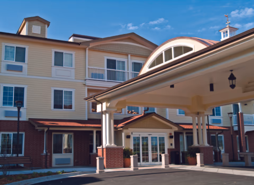 Front view of a beige senior living building with a covered entrance and columns.