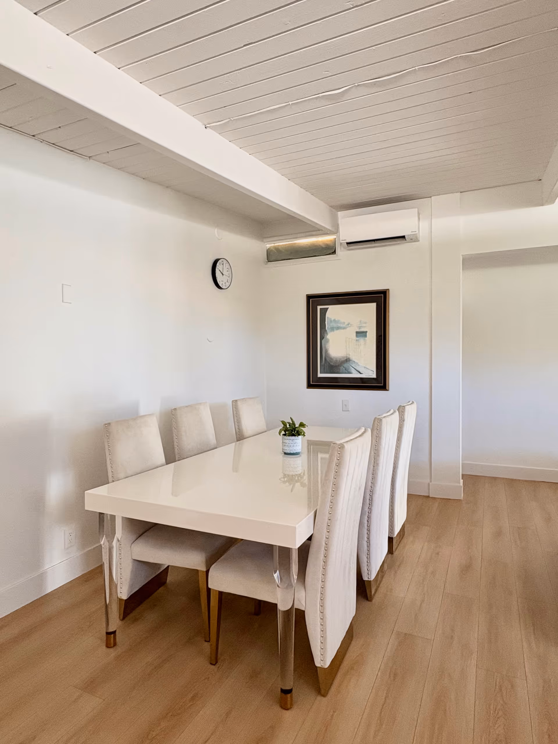 White dining table with six cream upholstered chairs in a bright, minimalist dining room.