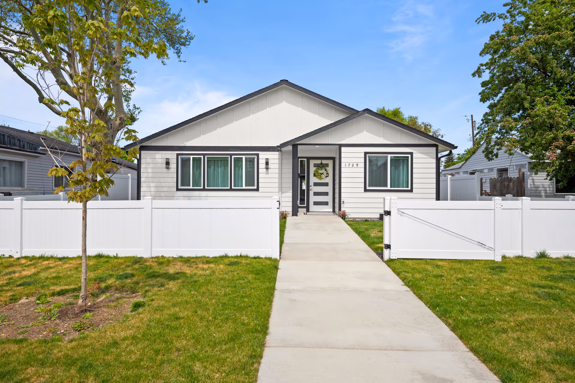 Front view of a single-story house with white fencing and a concrete walkway.