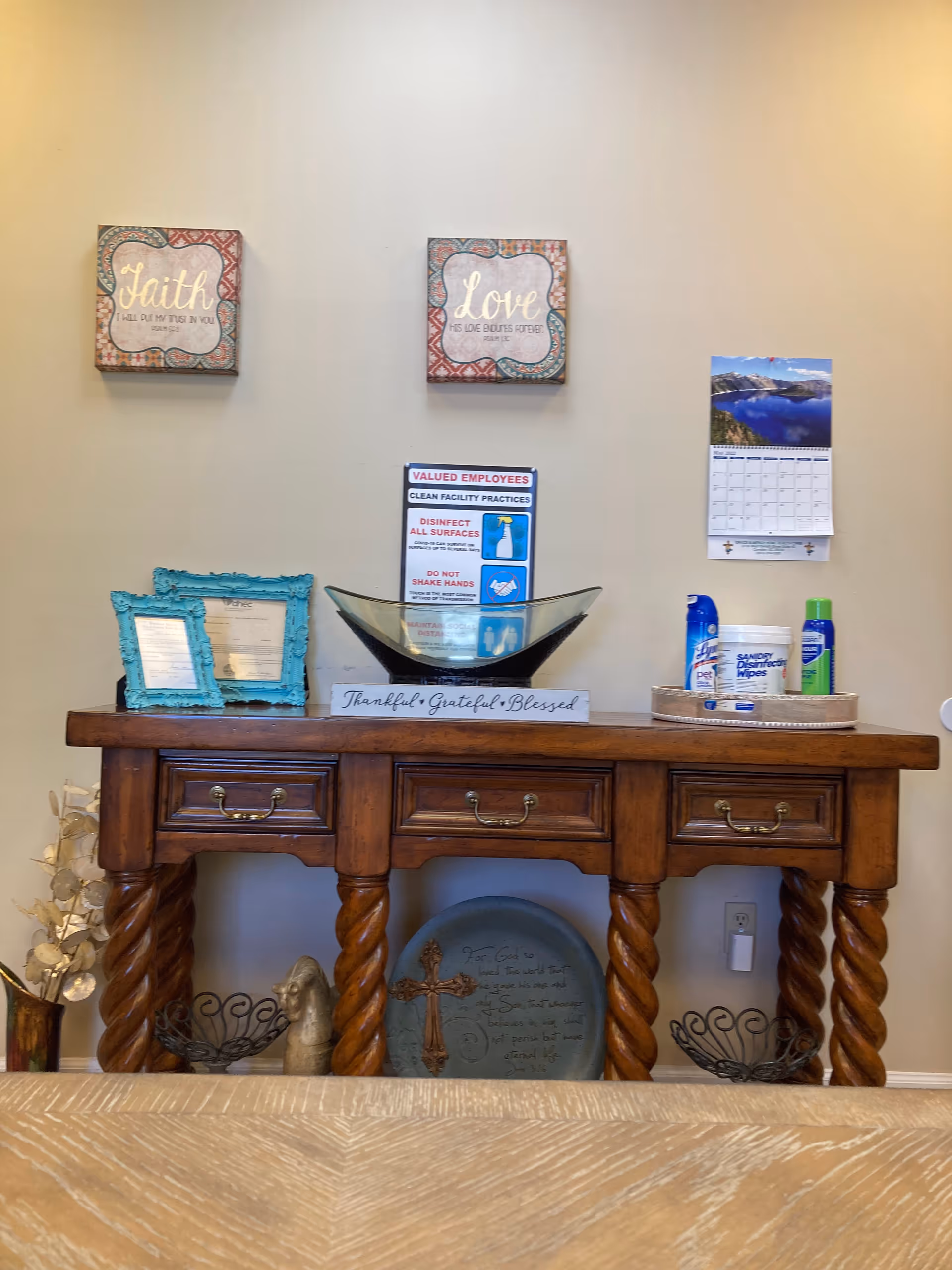 Wooden console table with decorative frames, a glass bowl centerpiece, and a Thankful Grateful Blessed sign.