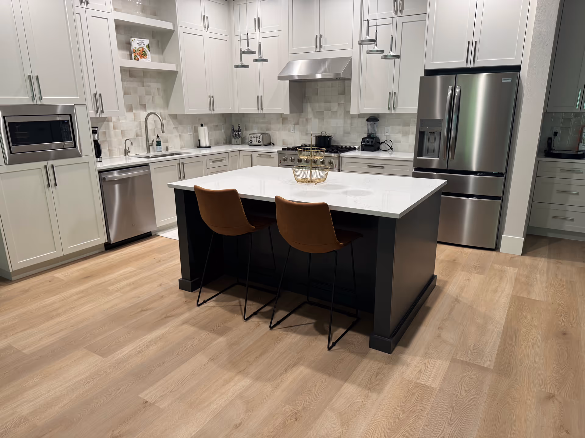 Modern white kitchen with island, stainless appliances, and light wood flooring.