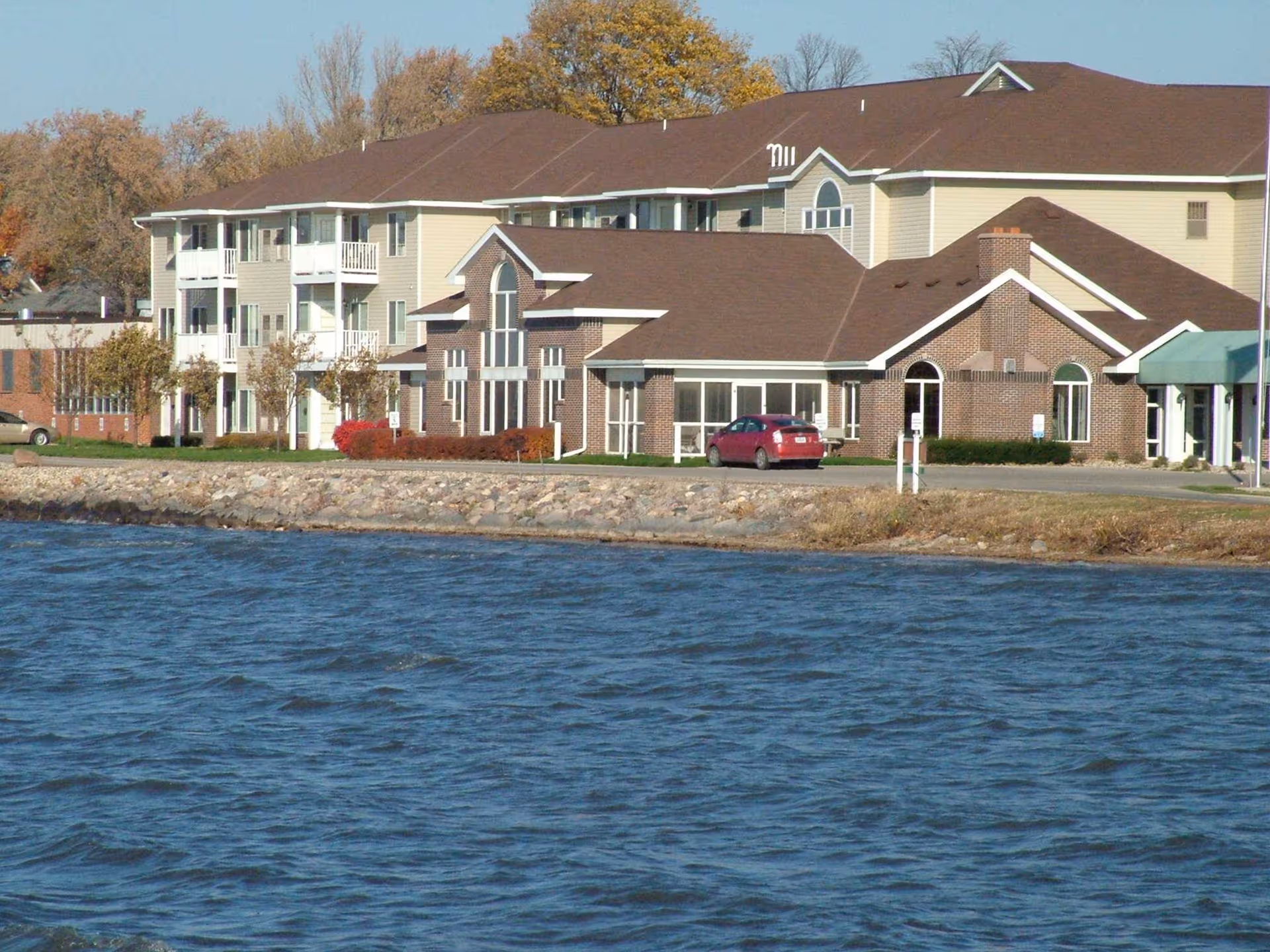 Methodist Manor senior living facility sits beside a waterfront, with autumn trees and a parking lot.