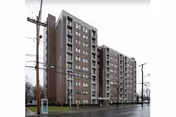A tall, multi-story brick building along a wet street, with power lines nearby.