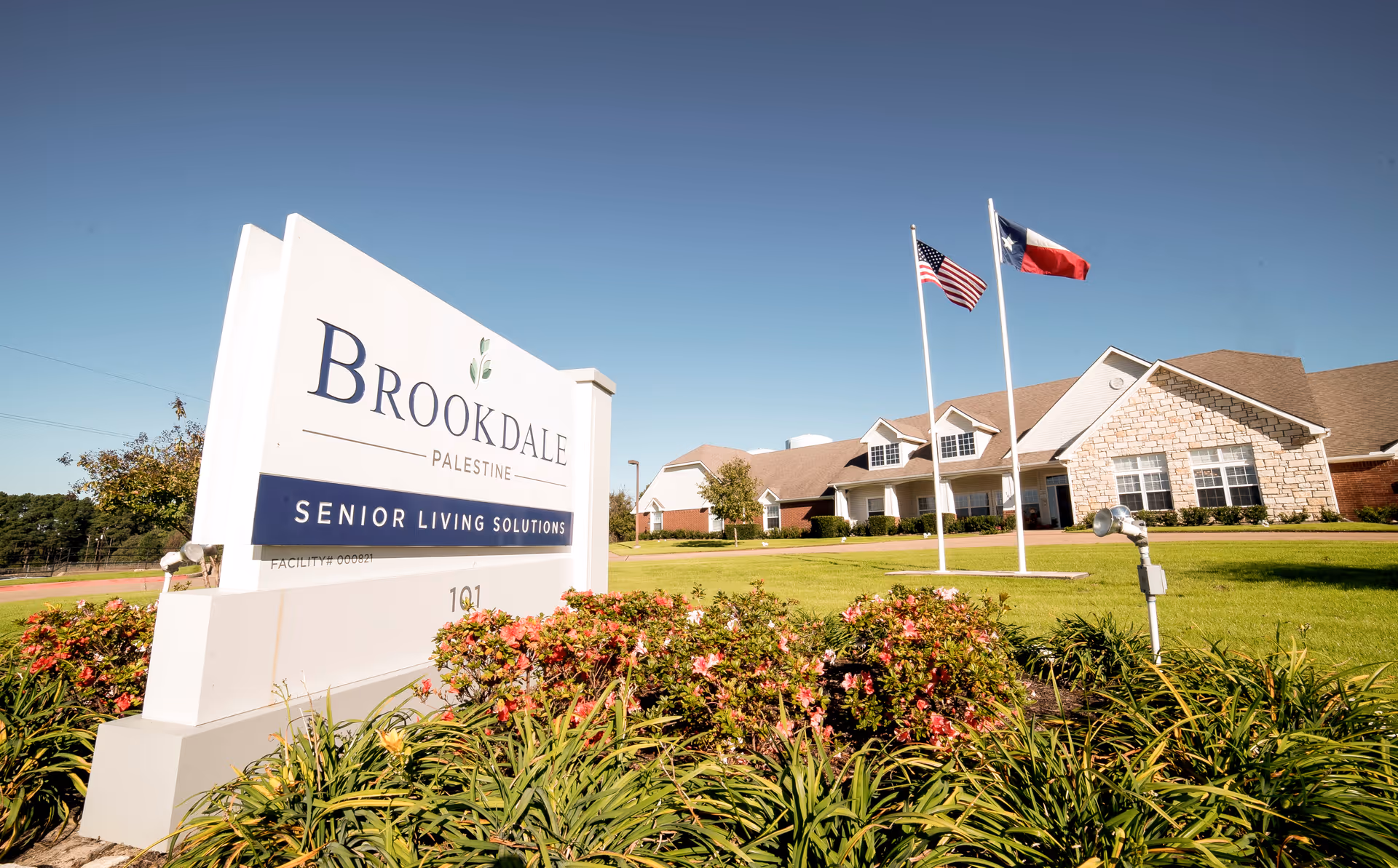 Exterior view of Brookdale Palestine senior living facility with sign, flags, and landscaped entrance.