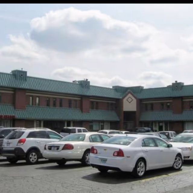 Exterior view of a senior care facility with a green roof and parked cars.
