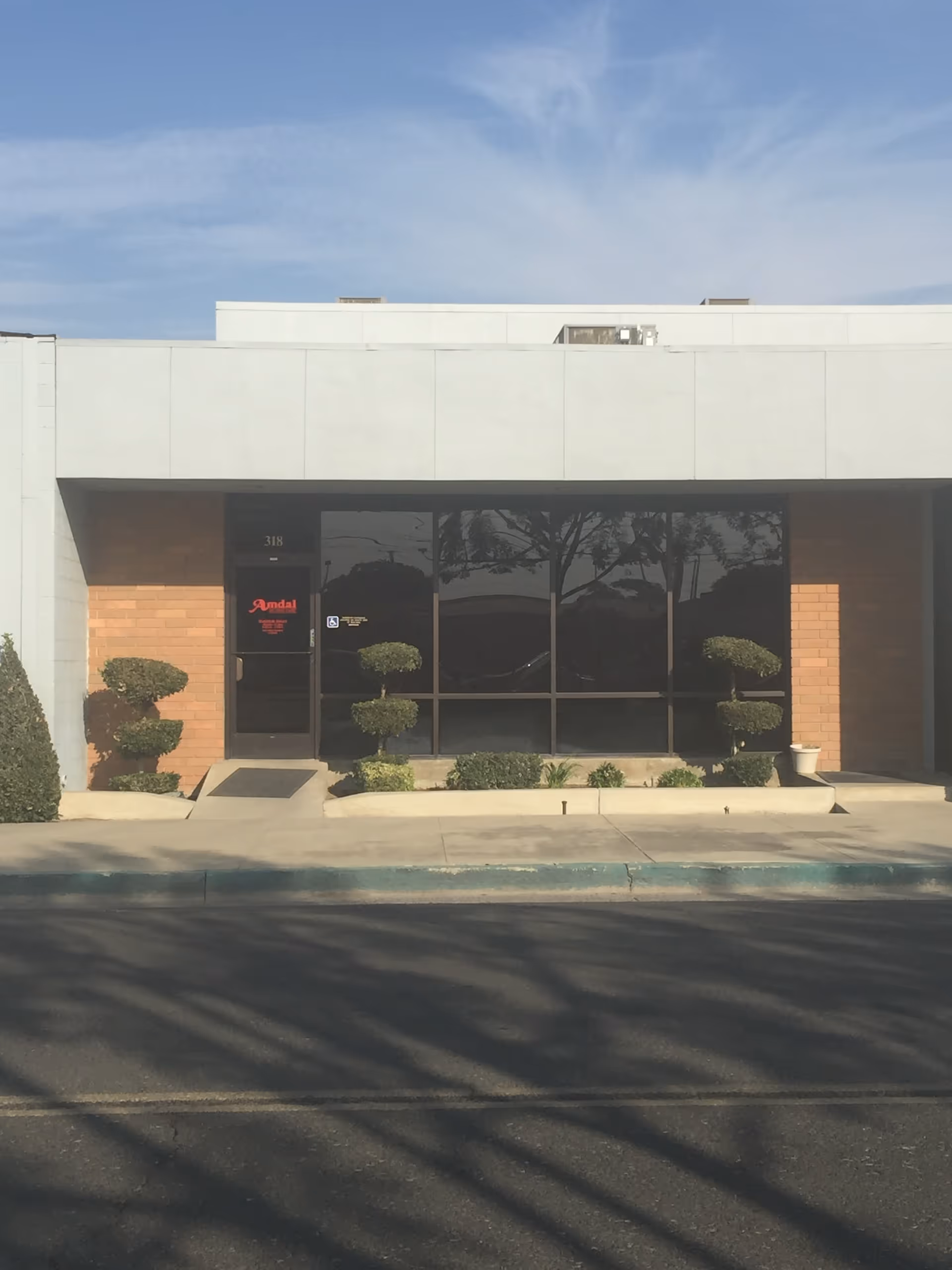 Front exterior of Amdal In-Home Care facility with glass doors and trimmed shrubs.