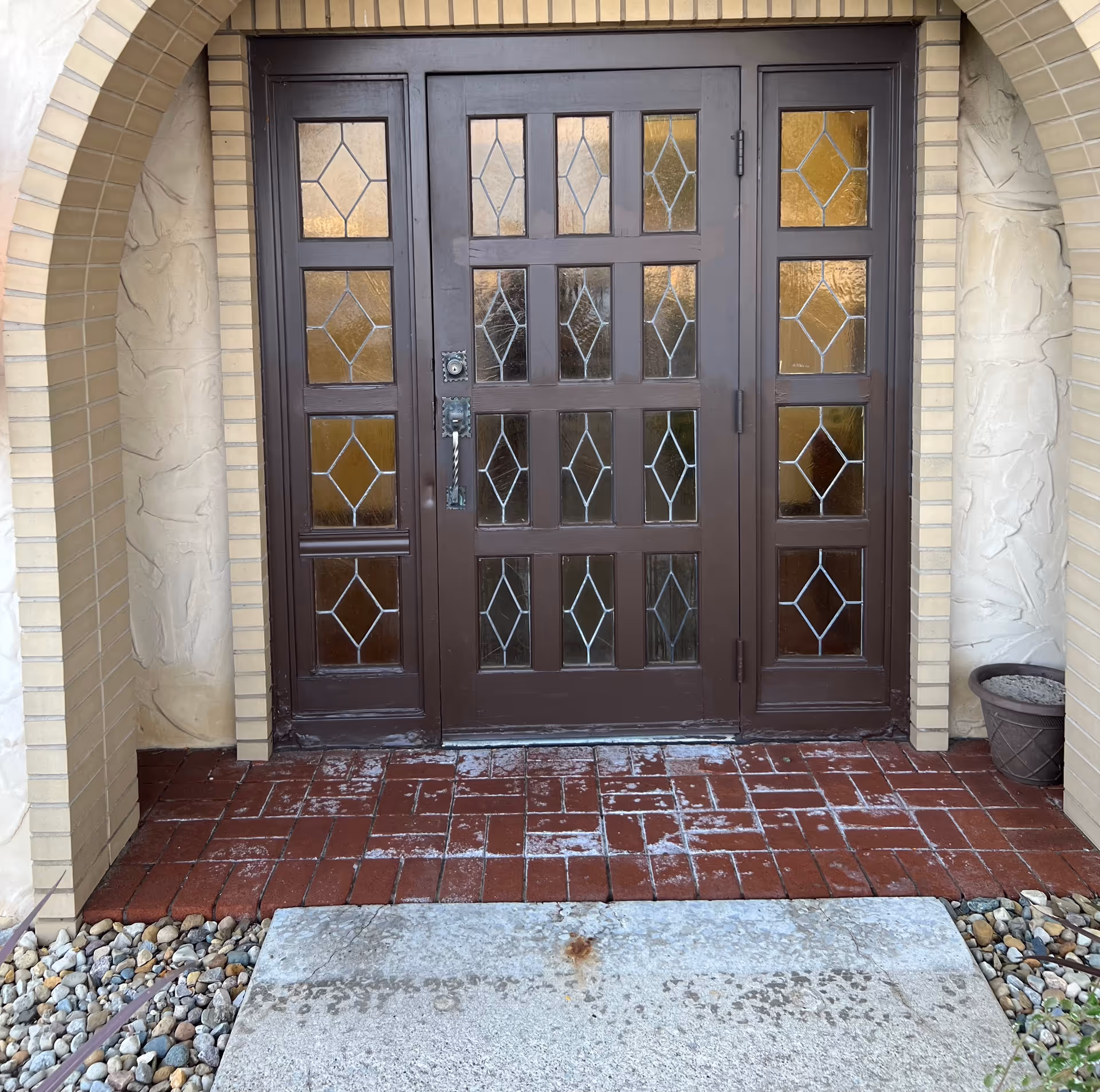 Dark brown door with glass panels, brick arch, and front steps.
