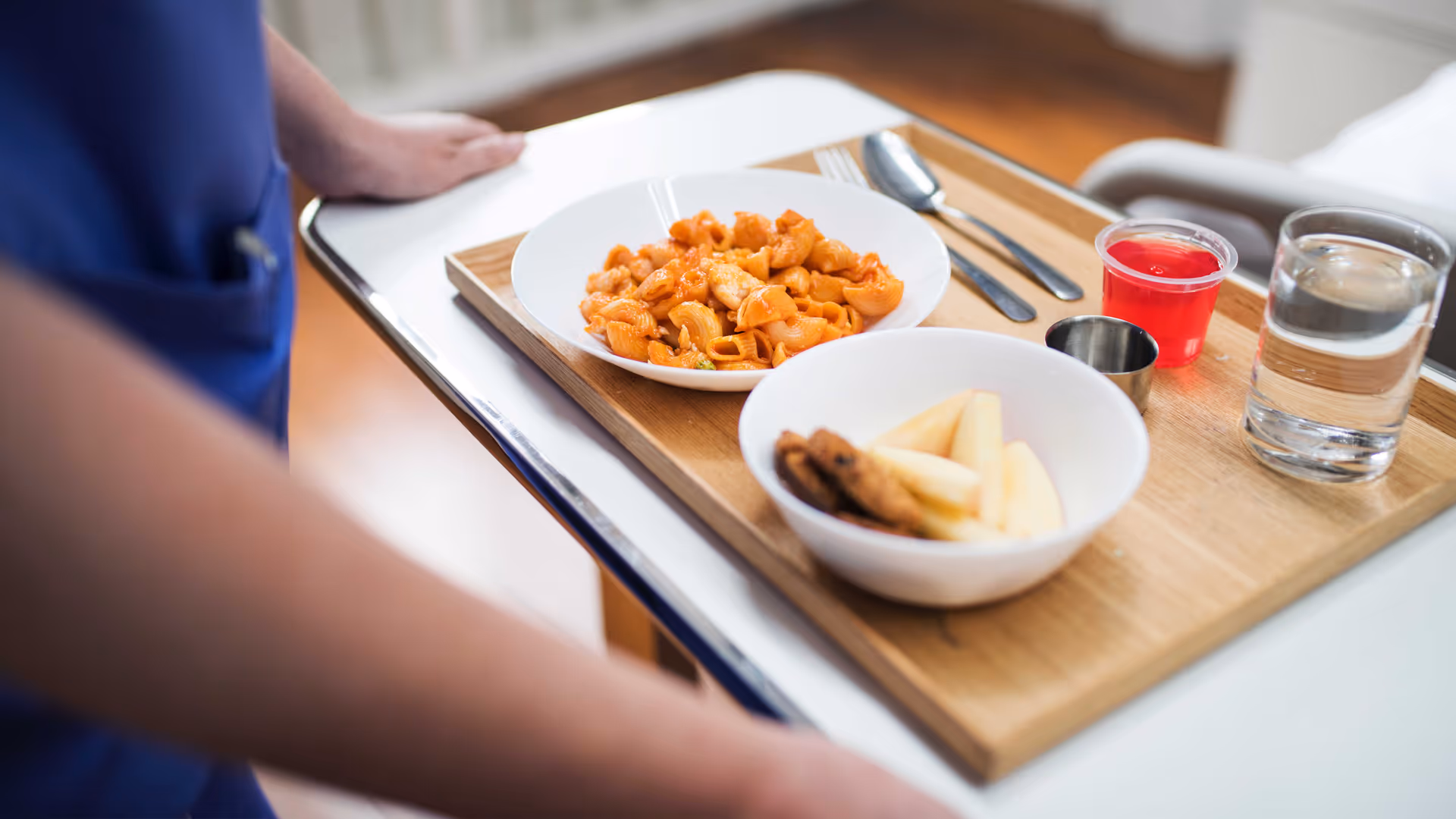 A dining tray with pasta, fries, and drinks on a wooden table in a dining area.